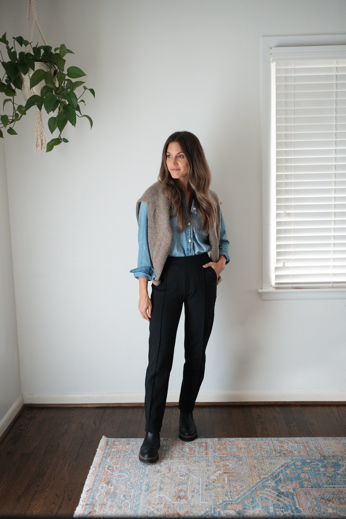 black pants outfit idea with a denim button down, sweater worn over the shoulders, and black Chelsea boots
