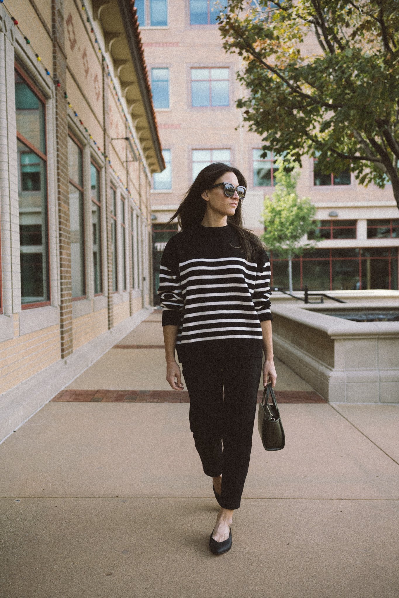 ashley wearing a black and white striped sweater, black pants, black slingback flats, and carrying an olive green handbag