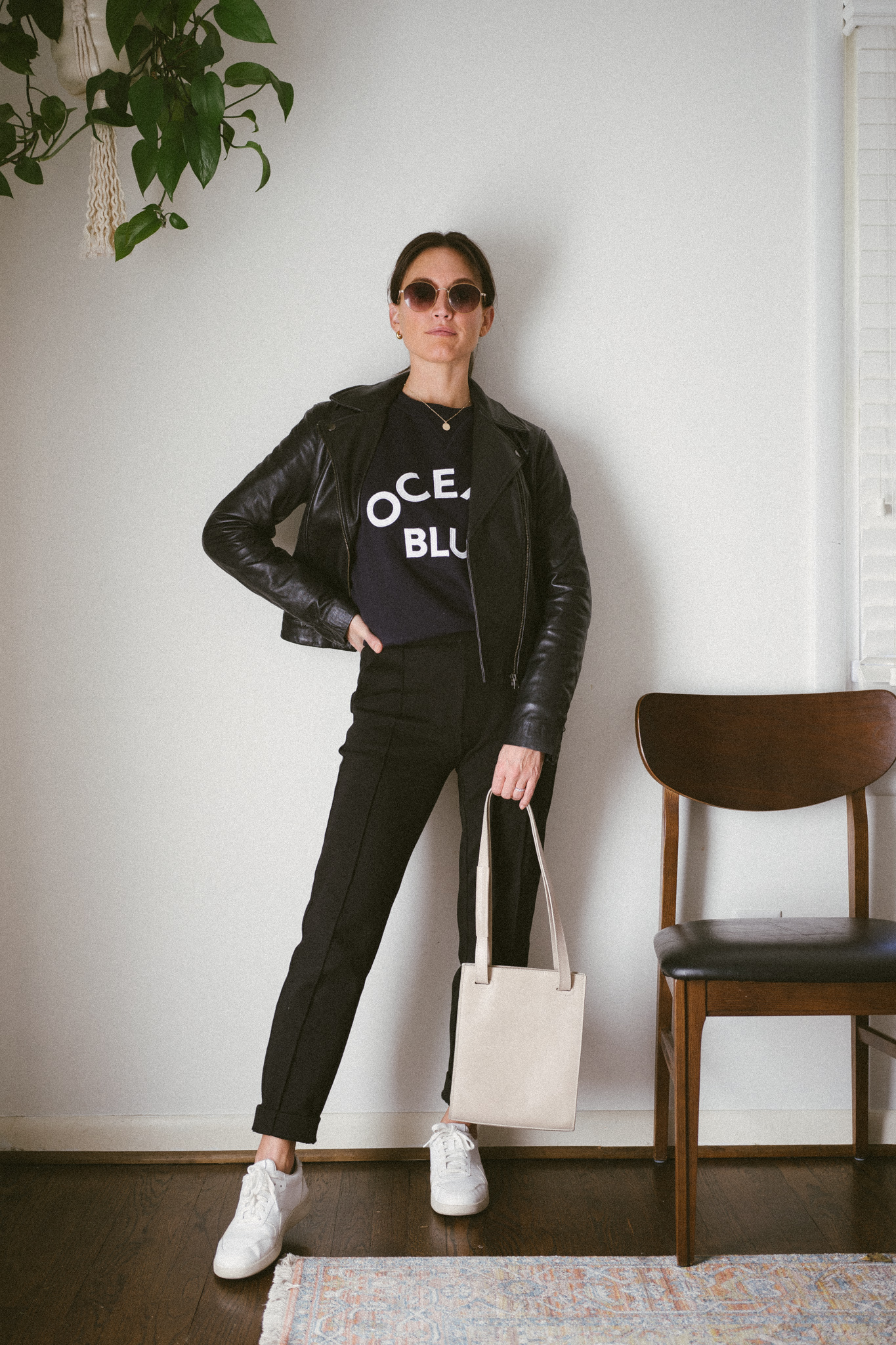 fall outfit idea with a navy graphic sweatshirt, leather jacket, black pants, and white sneakers