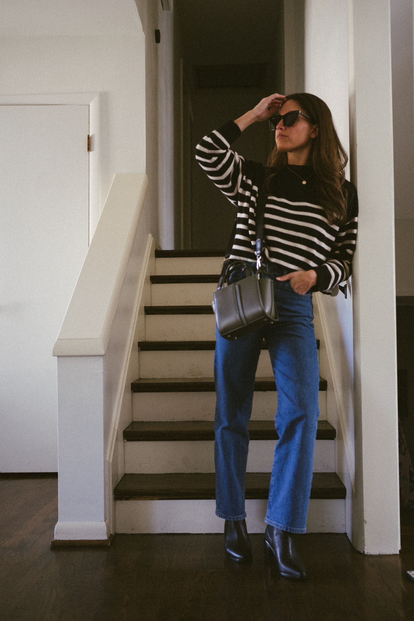 casual fall outfit with a black and white striped sweater, medium wash denin, and black boots