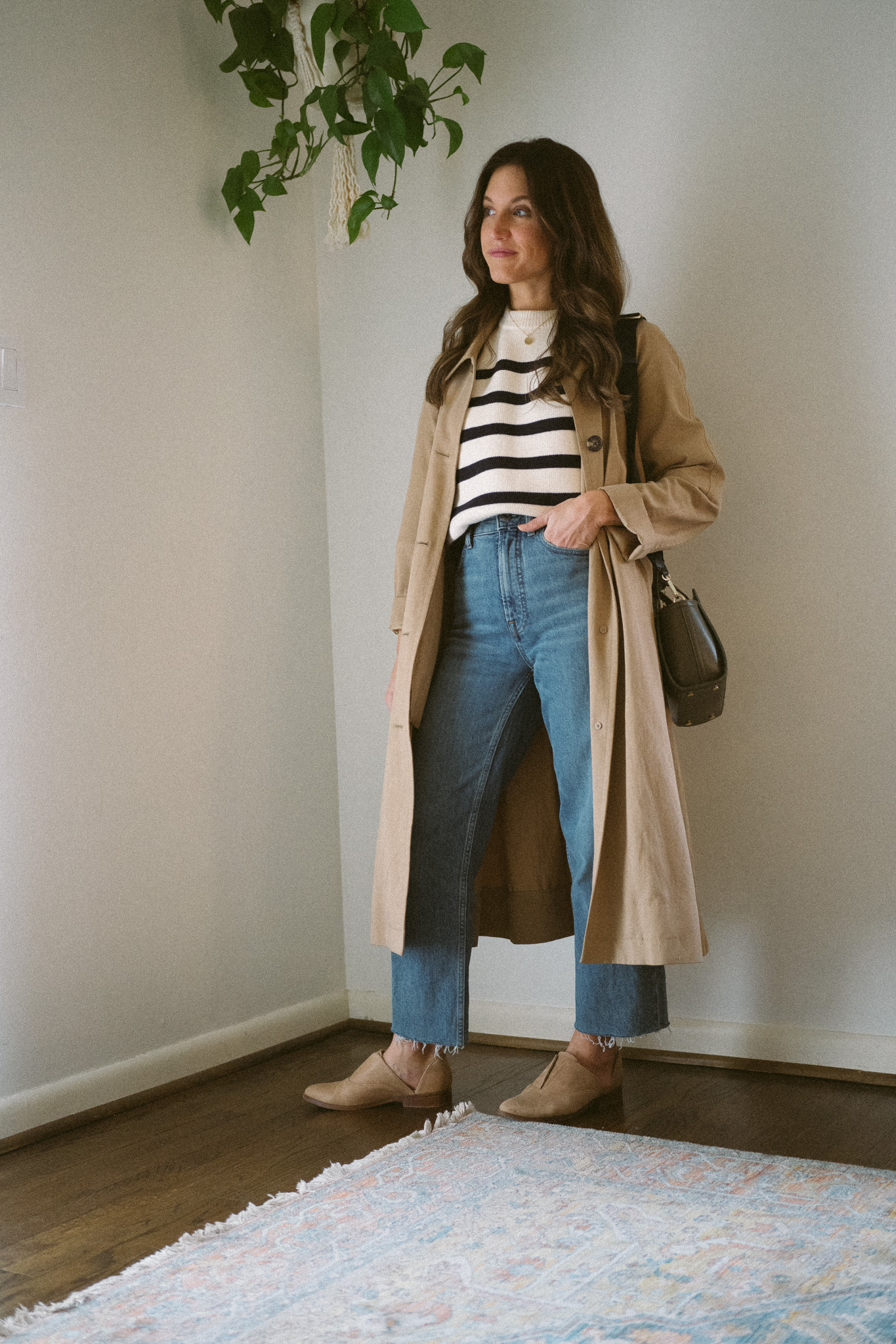 ashley wearing a cream and navy striped sweater, trench coat, medium wash straight denim, and tan Oxfords