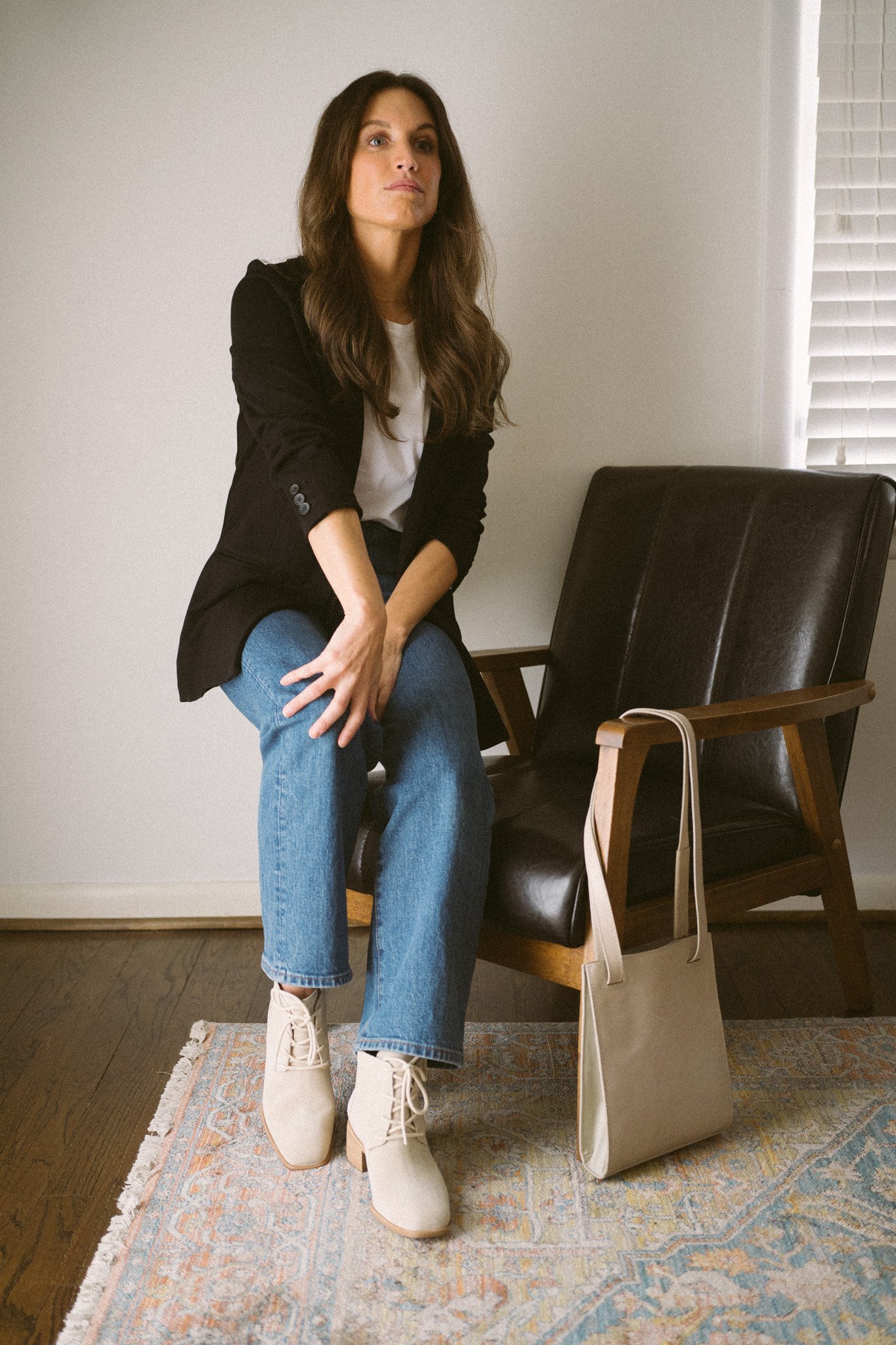 neutral fall outfit with a white tee, black blazer, medium wash denim, and light gray ankle boots