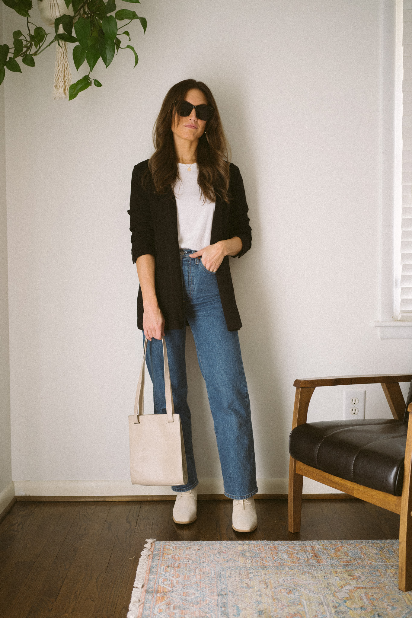 neutral fall outfit with a white tee, black blazer, medium wash denim, and light gray ankle boots