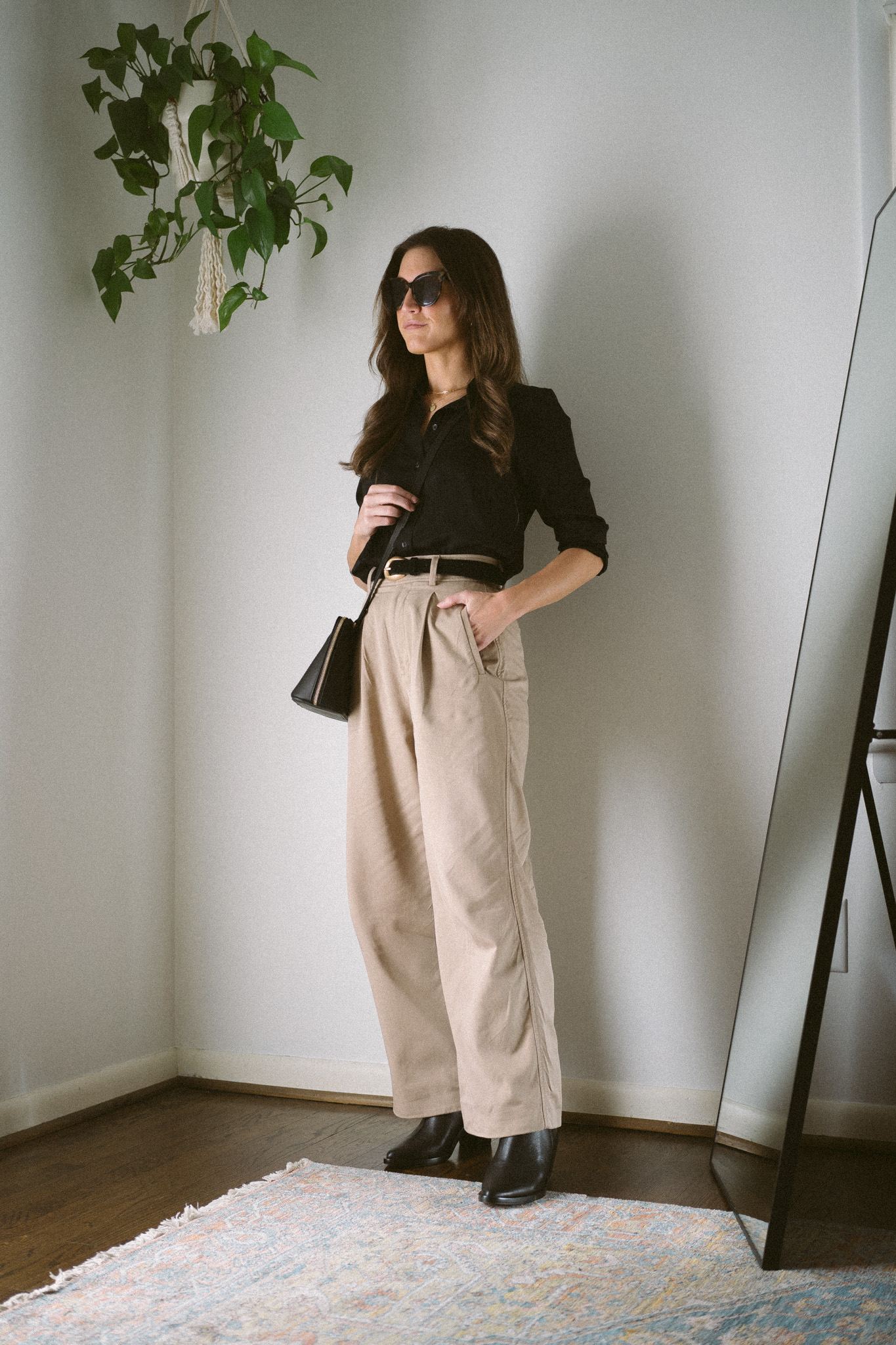 neutral fall outfit with a black silk top, tan wide leg trousers, and black heeled ankle boots