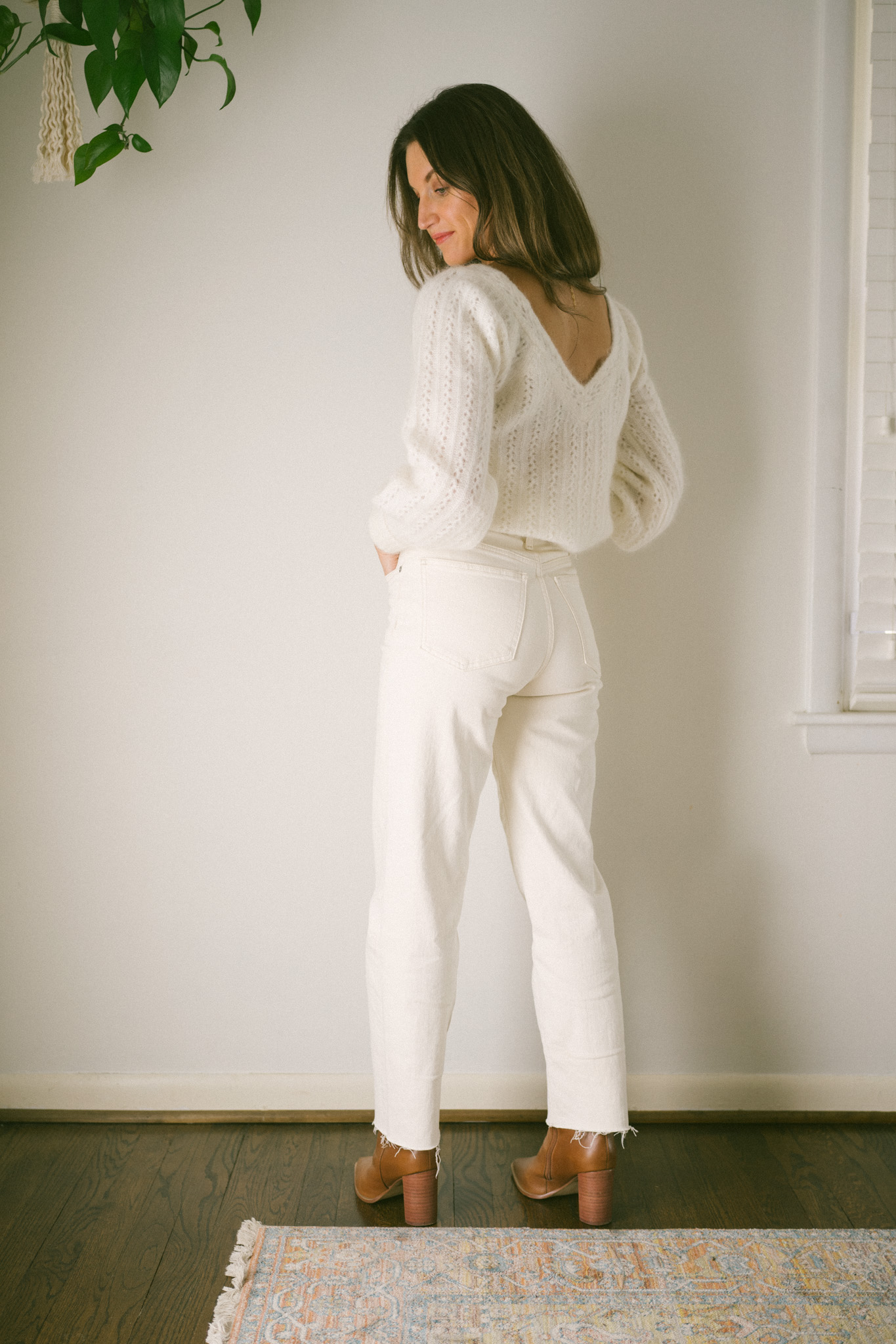 ashley wearing a white sweater with a v-neck back, white denim, and brown boots