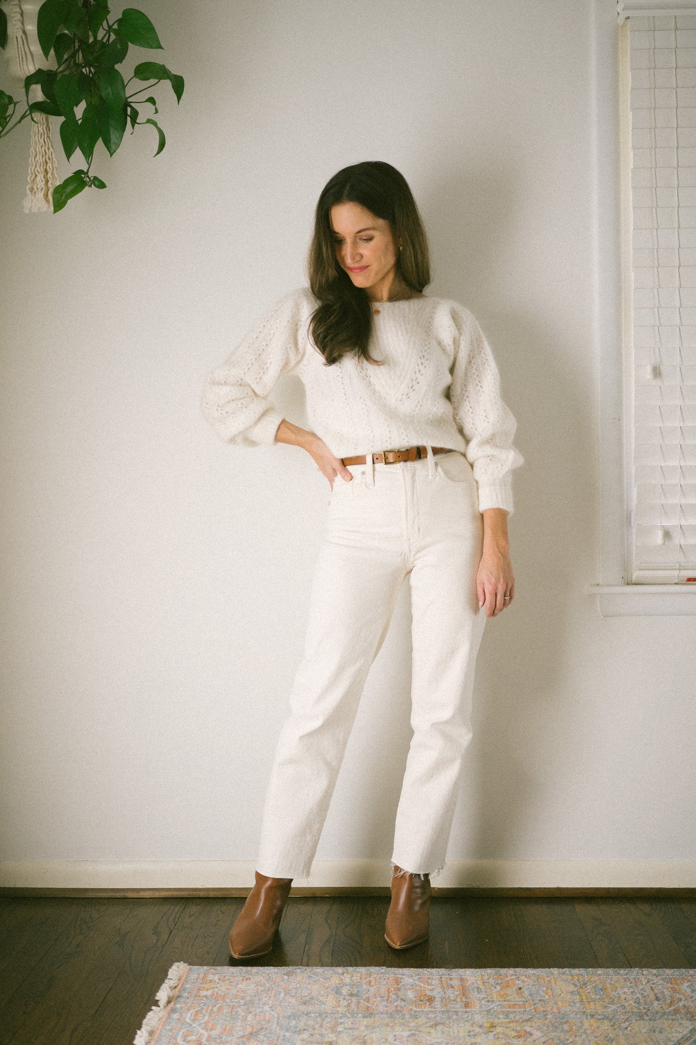 ashley wearing a white sweater, white denim, and brown boots and a brown belt