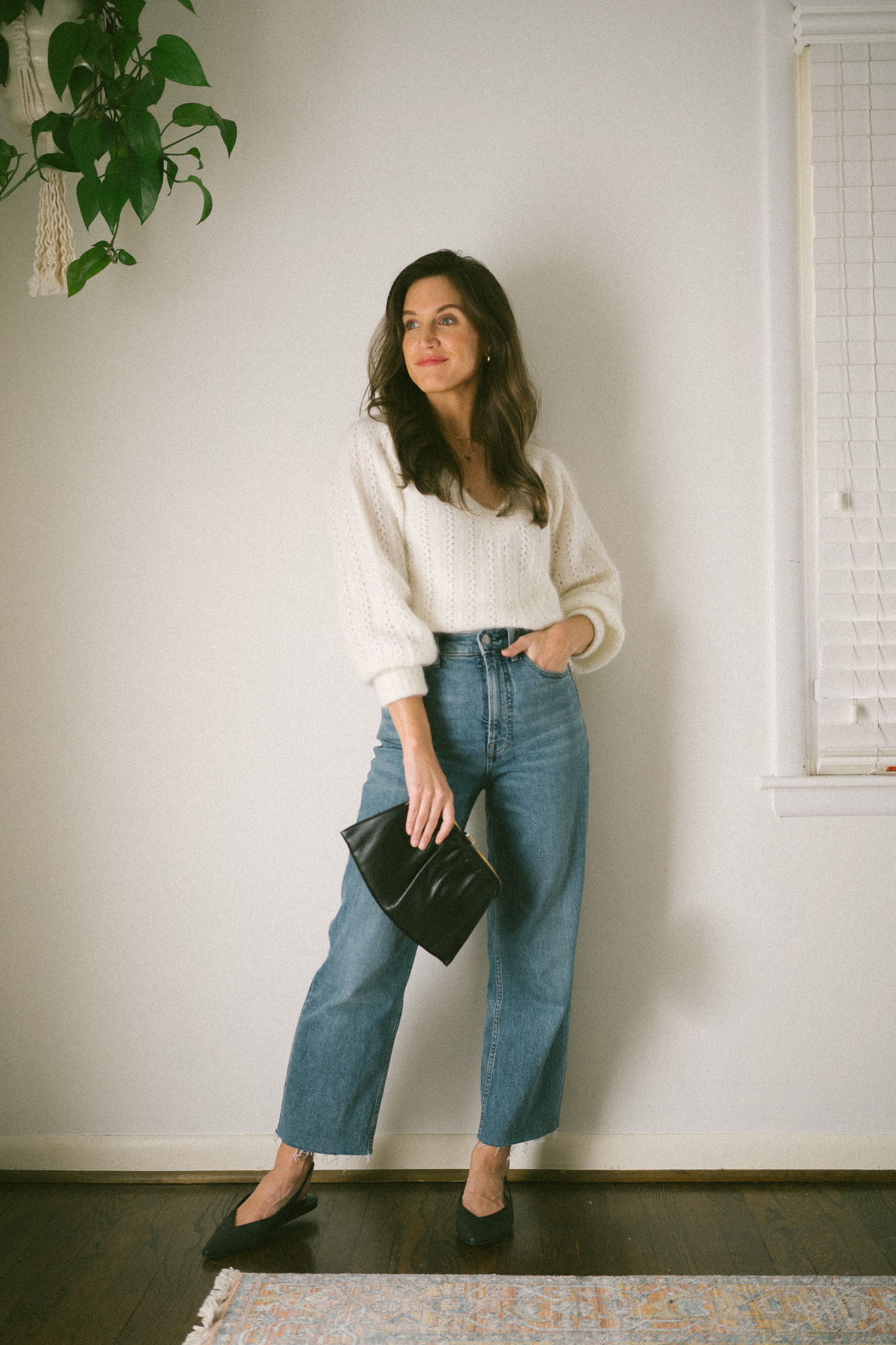 ashley wearing a white sweater, medium wash straight denim, black slingback flats and a vintage clutch bag