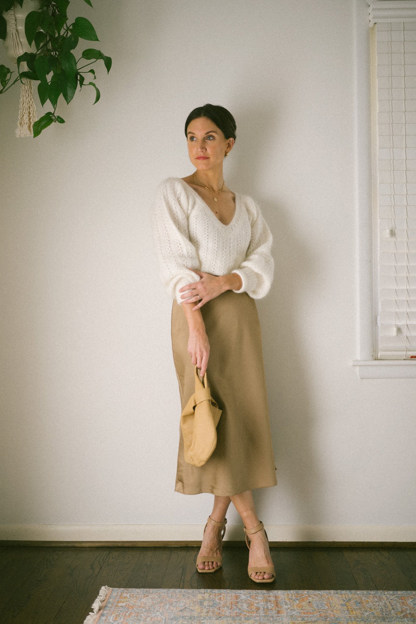 ashley wearing a white sweater, champagne colored slip skirt, nude heels, and a brown clutch bag