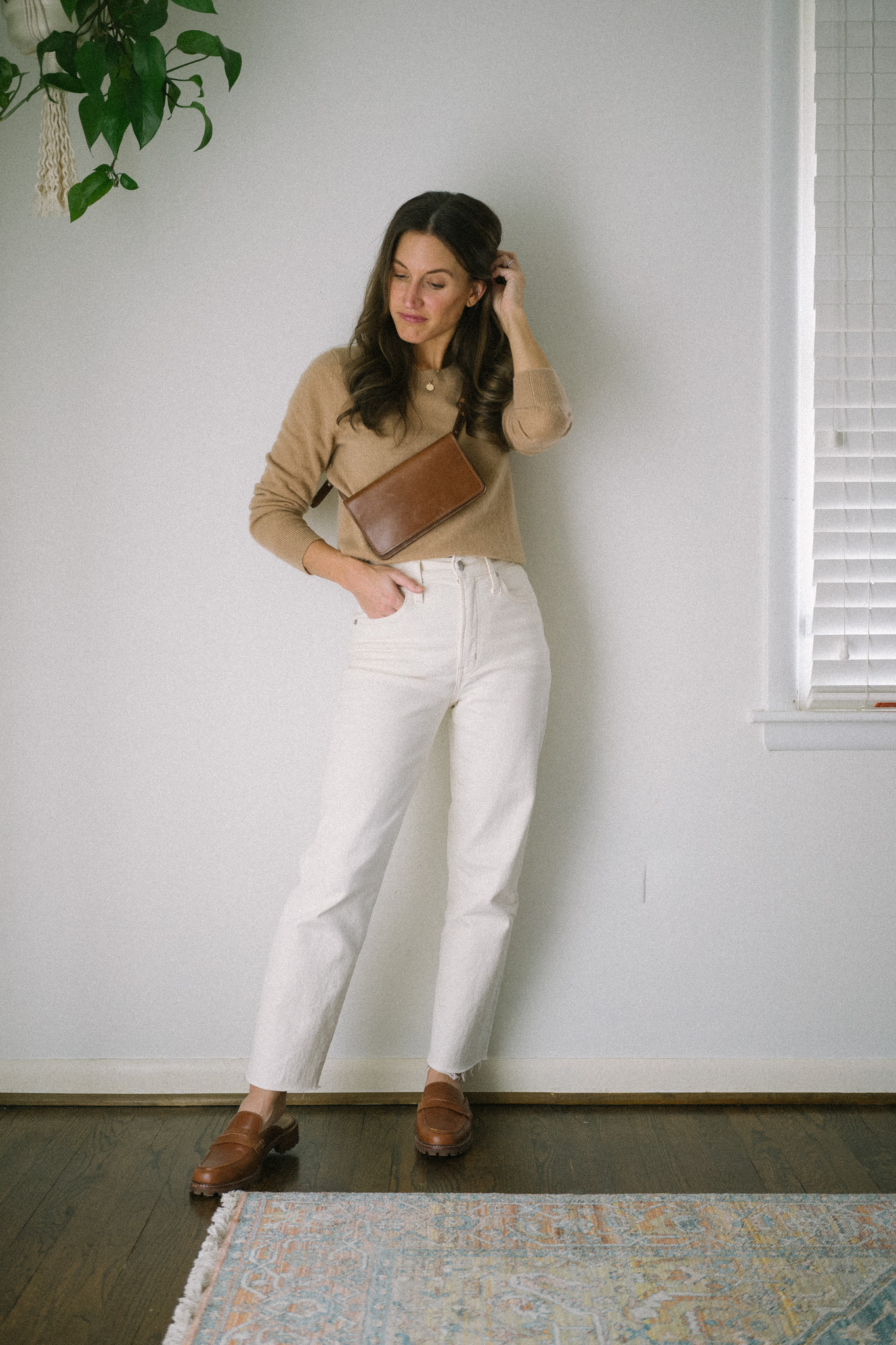 ashley wearing a camel sweater, white denim, and brown leather loafer mules
