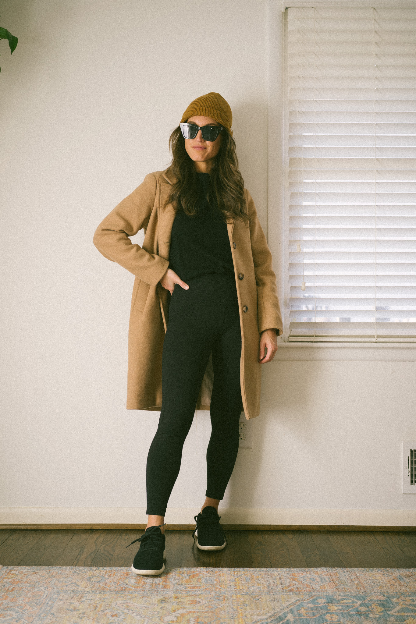 casual fall outfit with a black sweatshirt, black leggings, camel coat, and black sneakers
