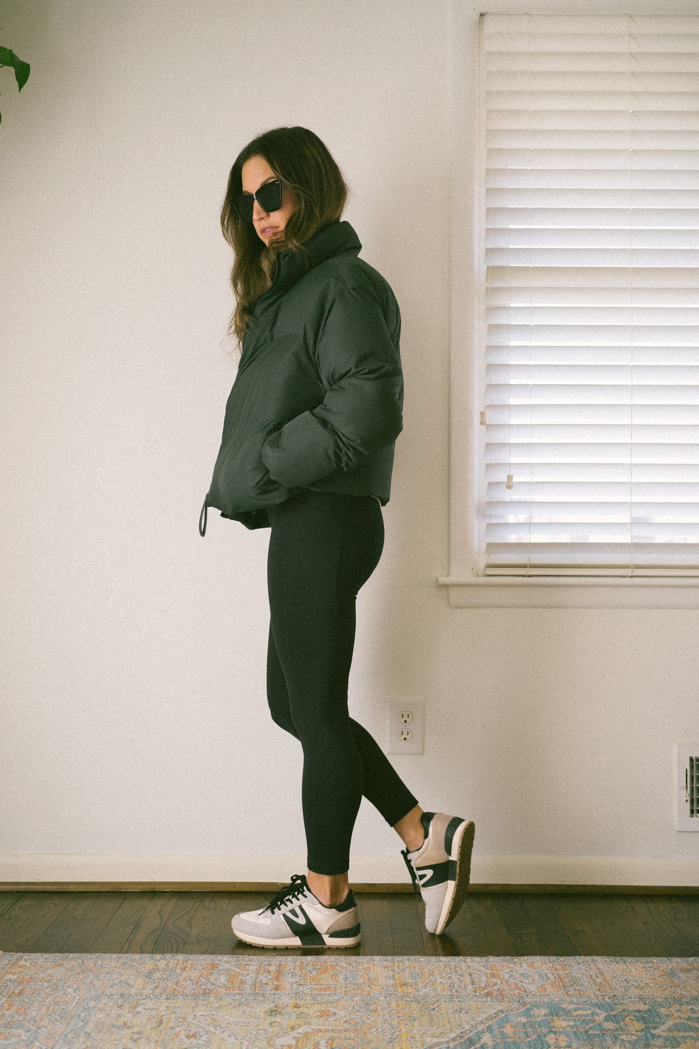 ashley wearing a casual fall outfit with a black cropped puffer, leggings, and casual neutral sneakers