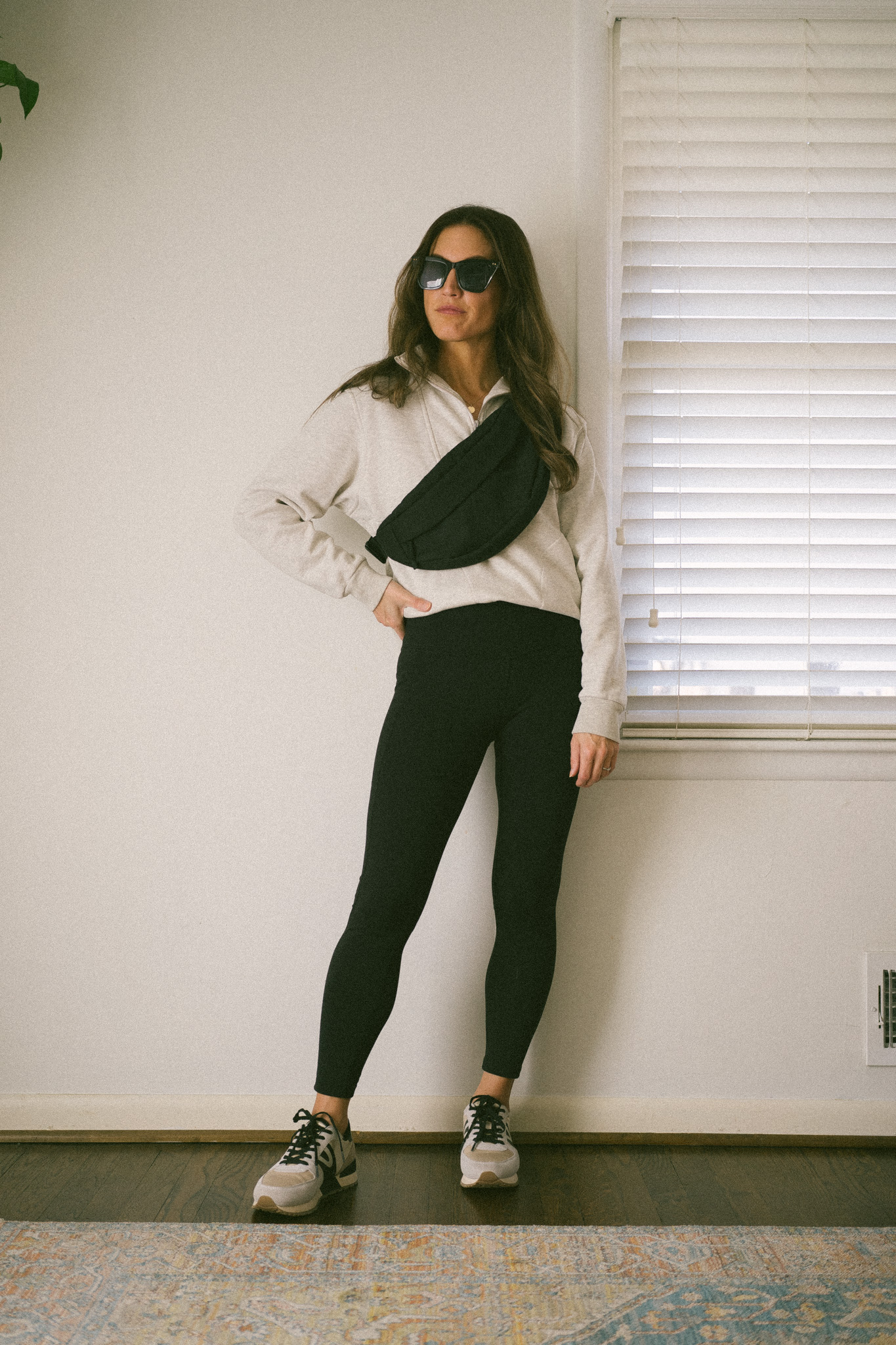 casual fall outfit with a gray half-zip sweatshirt, black leggings, casual colorblock sneakers, and a black belt bag
