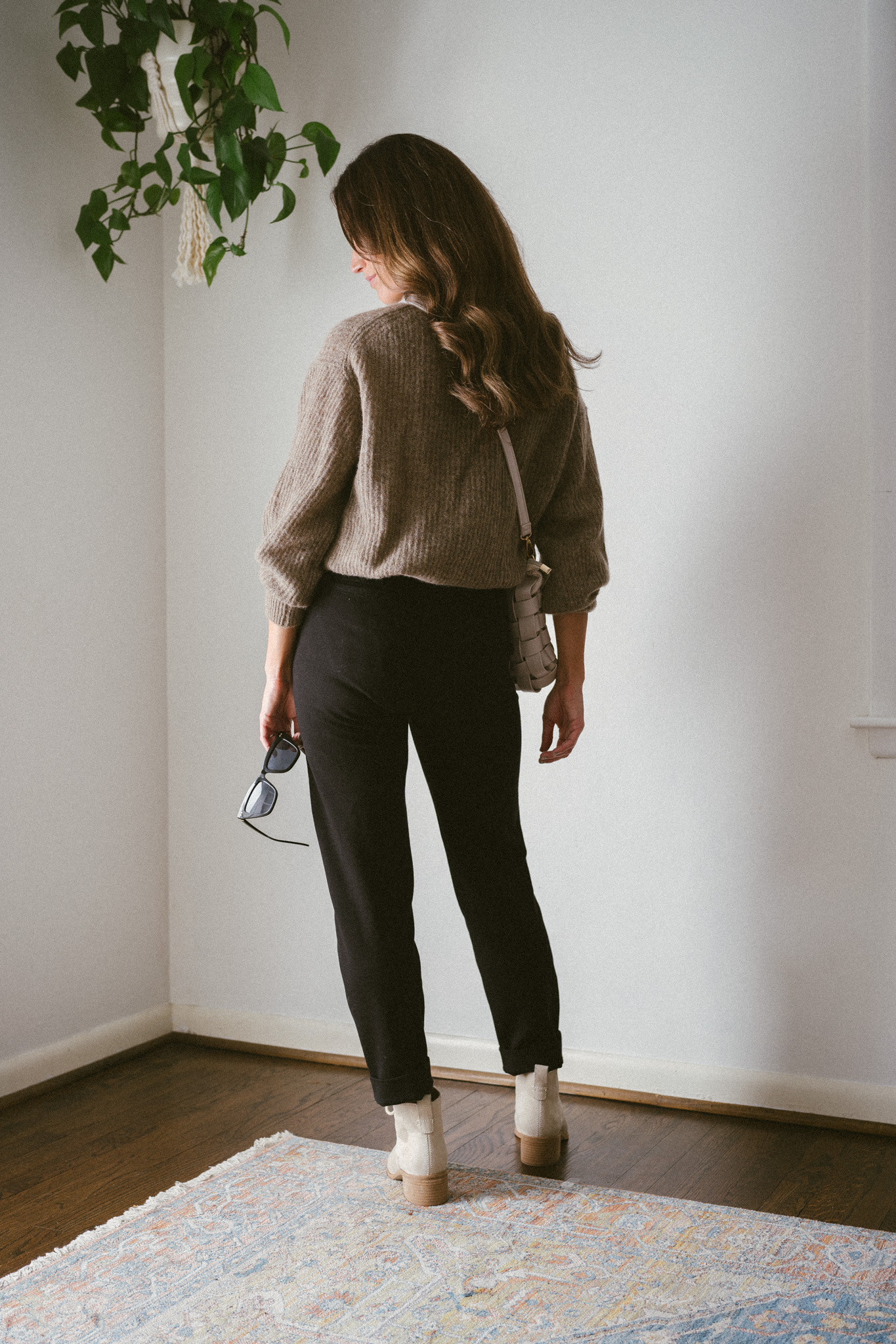 ashley wearing a taupe oversized sweater, black pants, and bone colored boots with laces with a woven bone colored bag and black sunglasses