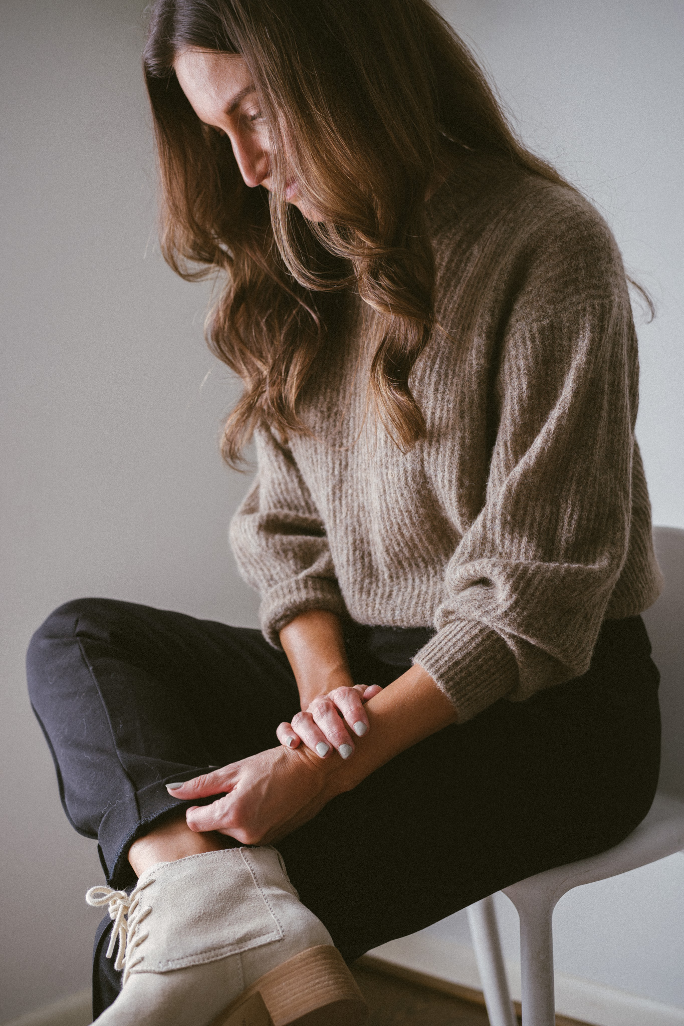 ashley wearing a taupe oversized sweater, black pants, and bone colored boots with laces with a woven bone colored bag and black sunglasses