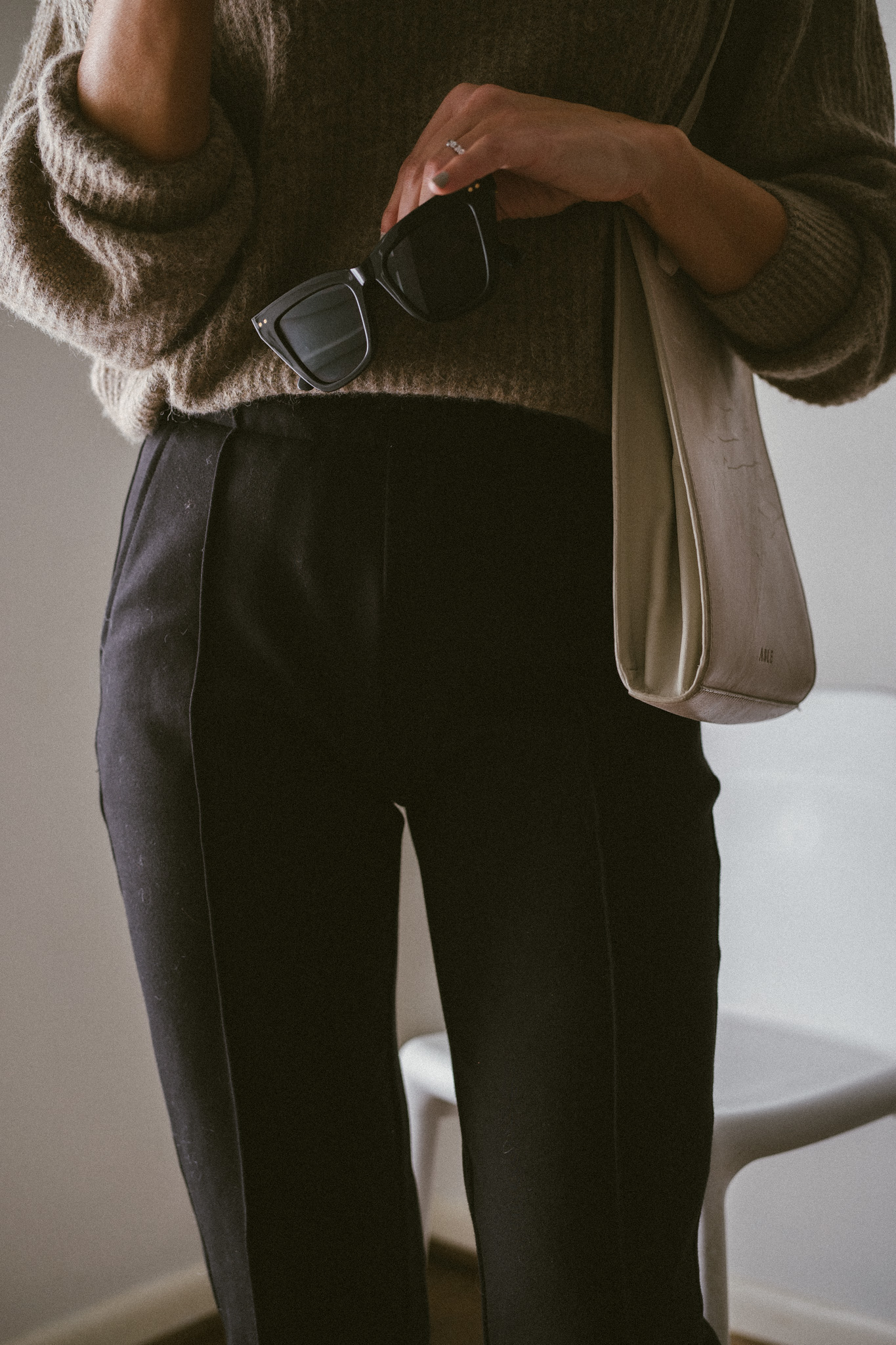 ashley wearing a taupe oversized sweater, black pants, and bone colored boots with laces with a woven bone colored bag and black sunglasses