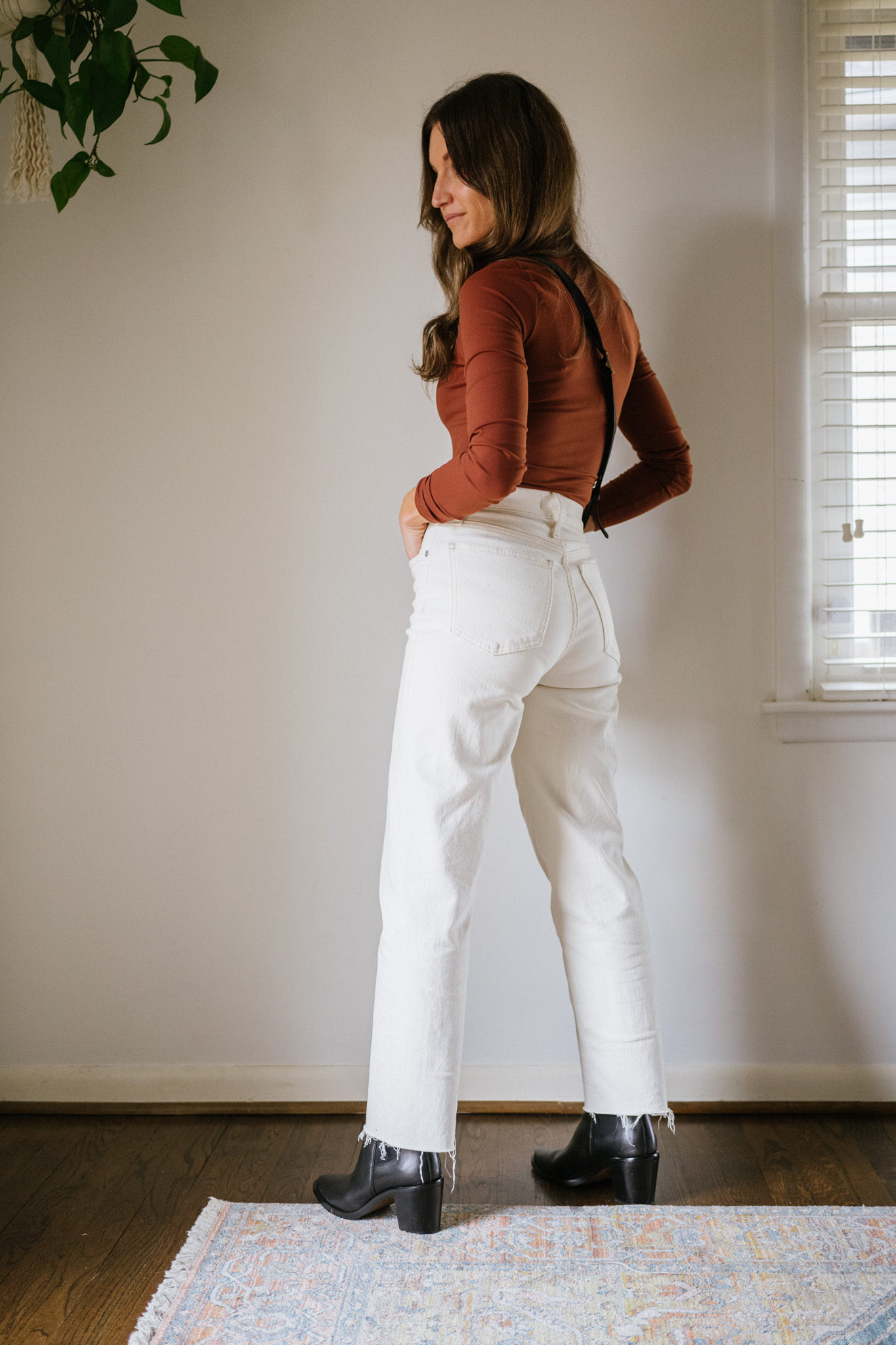 ashley wearing a reddish brown bodysuit and white jeans and black boots
