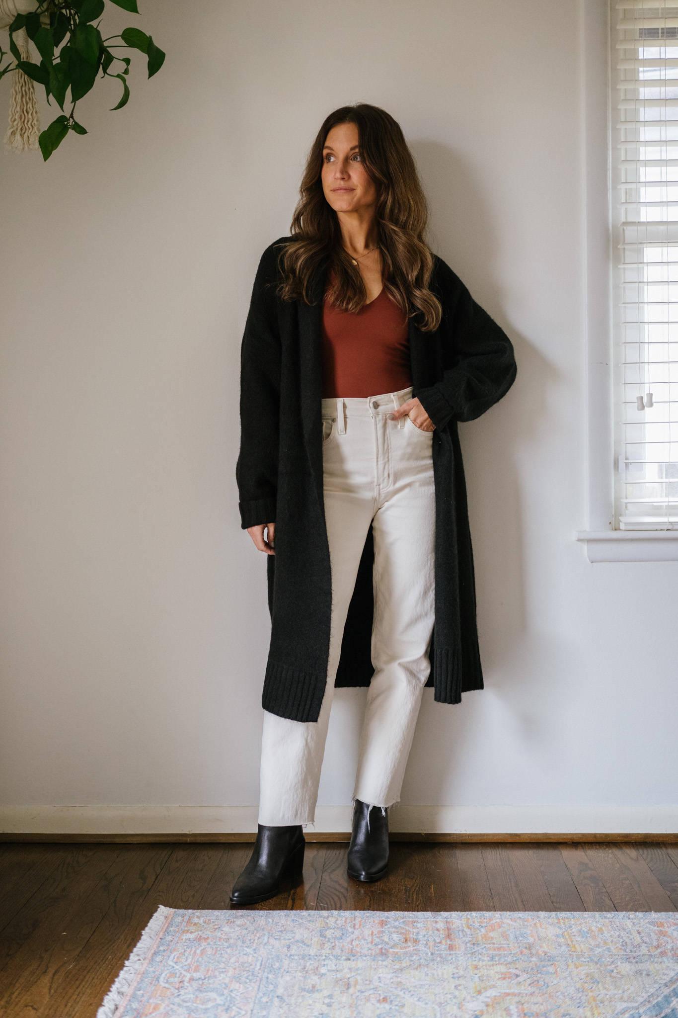 ashley wearing a reddish brown bodysuit and white jeans with an oversized cardigan, and black boots