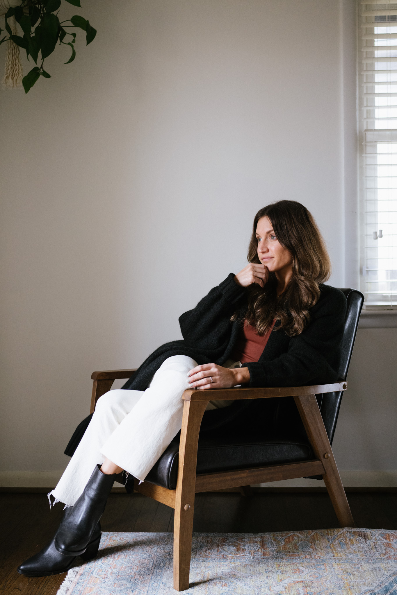 ashley wearing a reddish brown bodysuit and white jeans sitting in a black leather chair