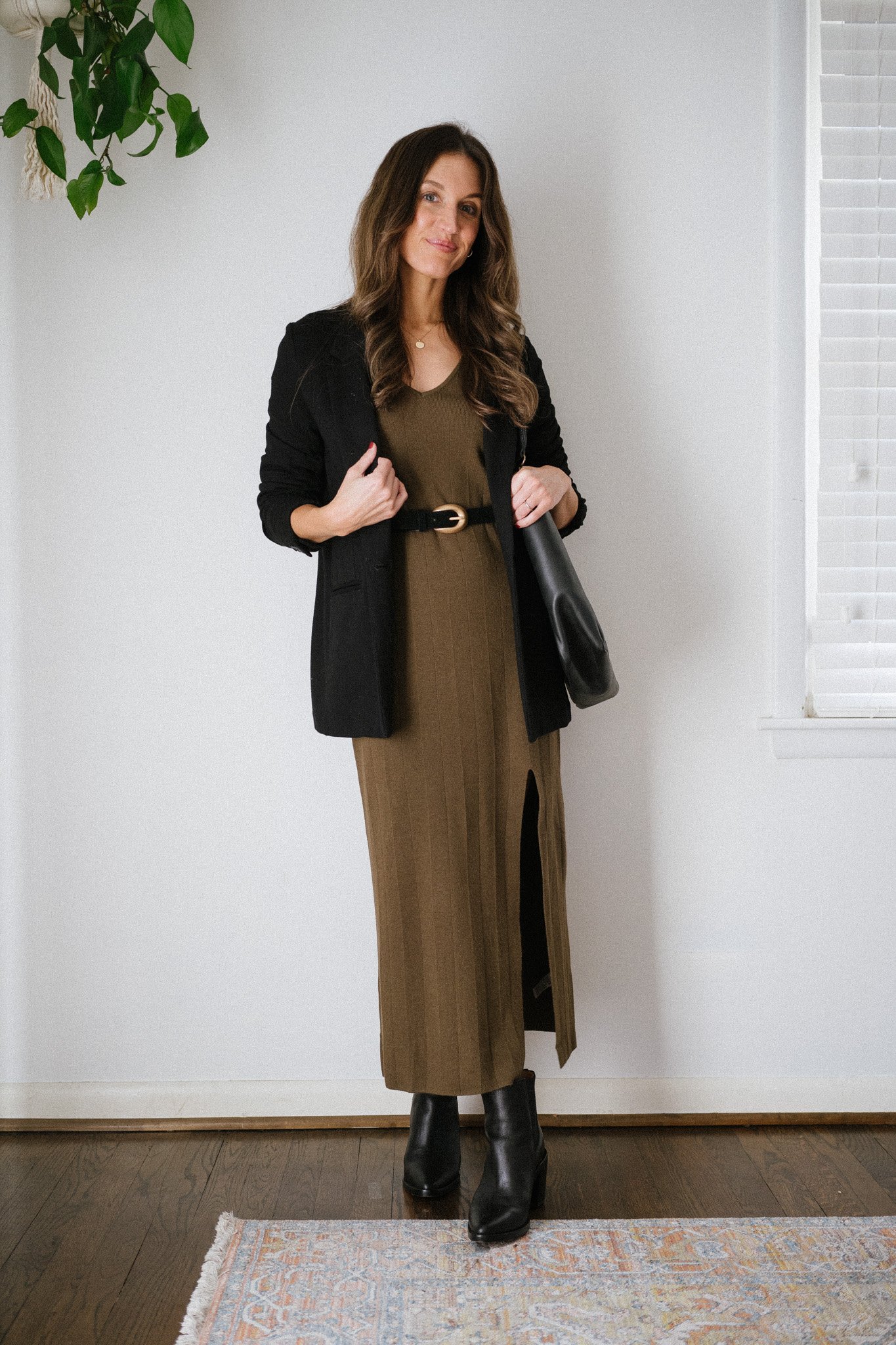 ashley wearing a green knit midi dress, black blazer, black belt, black heeled ankle boots, and a black tote bag