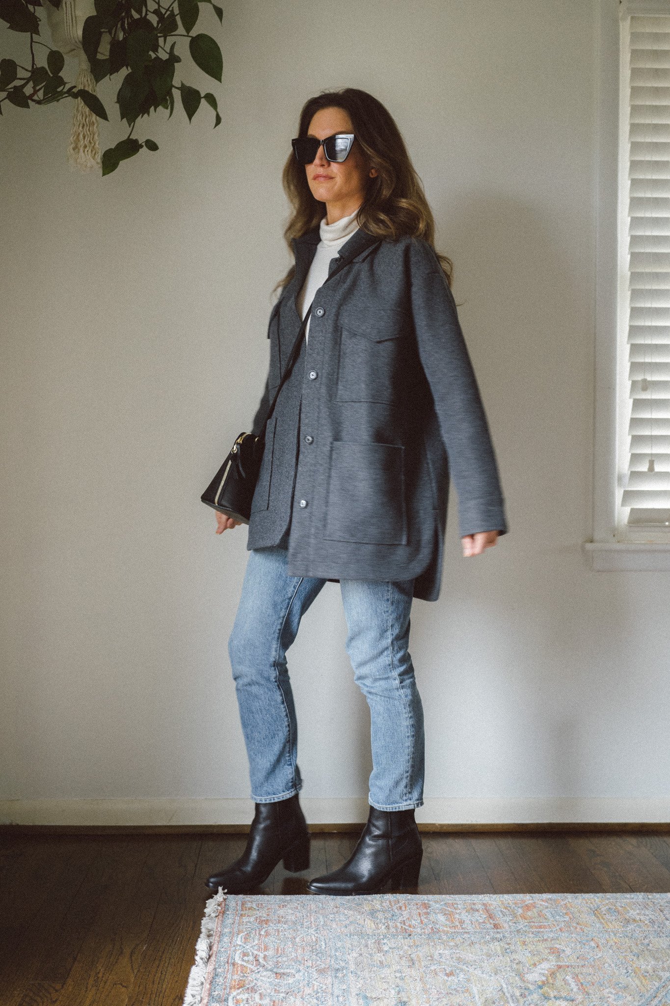 casual chic outfit idea with a cream colored turtleneck, gray shacket, medium wash denim, and black ankle boots