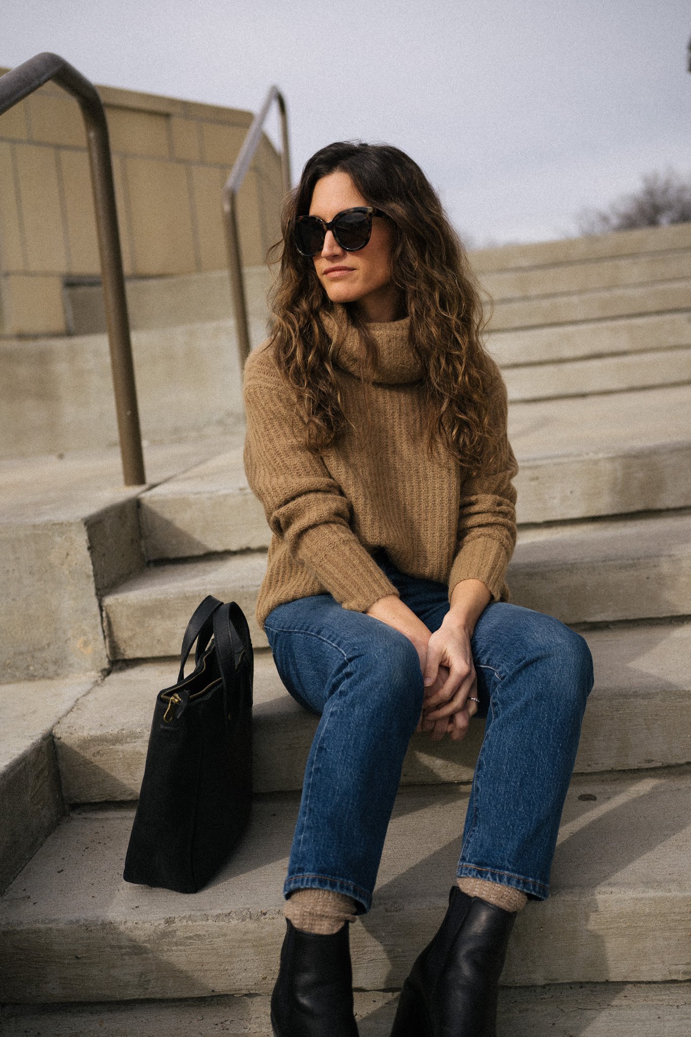 ashley wearing a brown turtleneck sweater, dark wash denim, and black boots