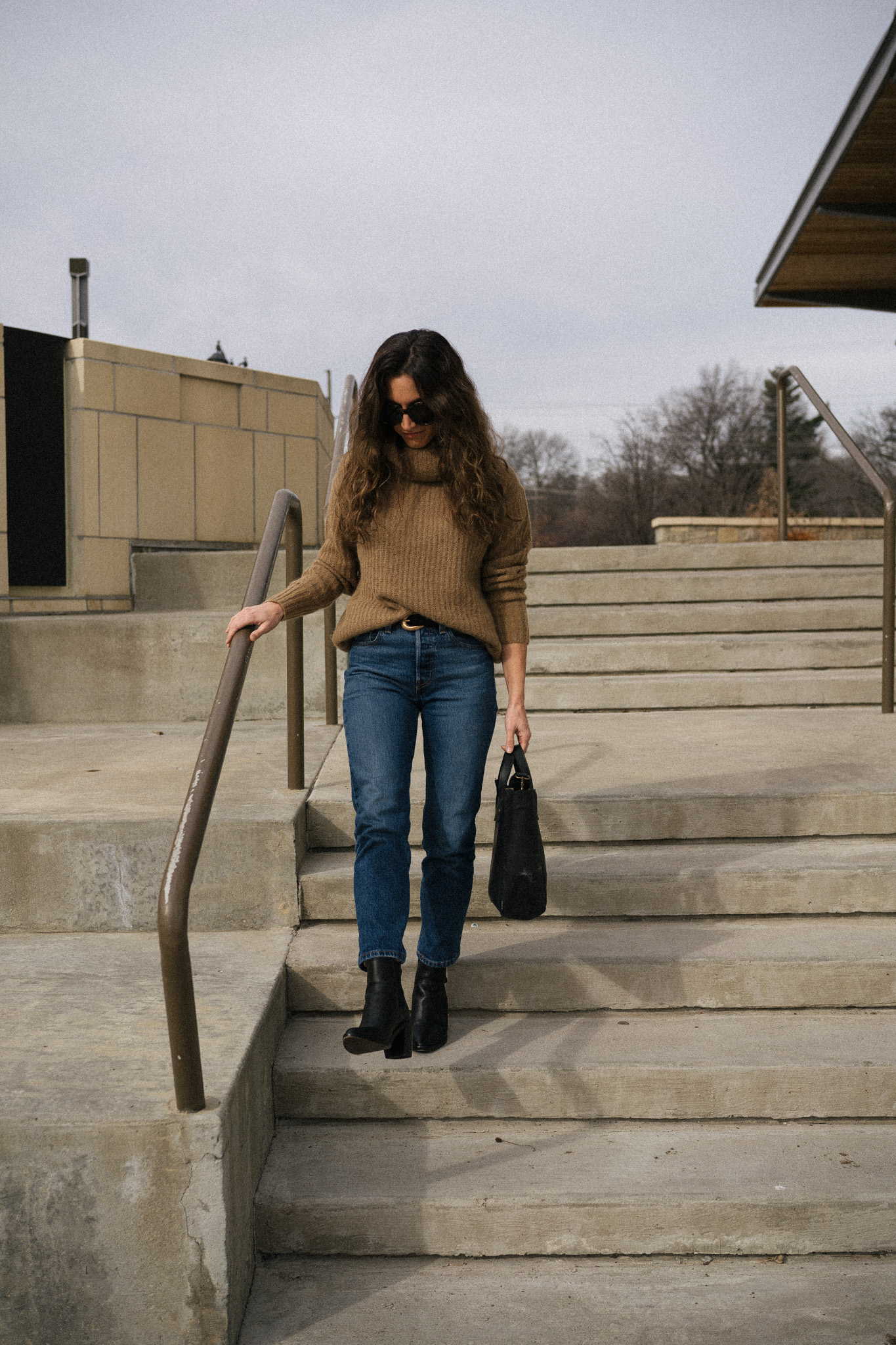ashley wearing a brown turtleneck sweater, dark wash denim, and black boots