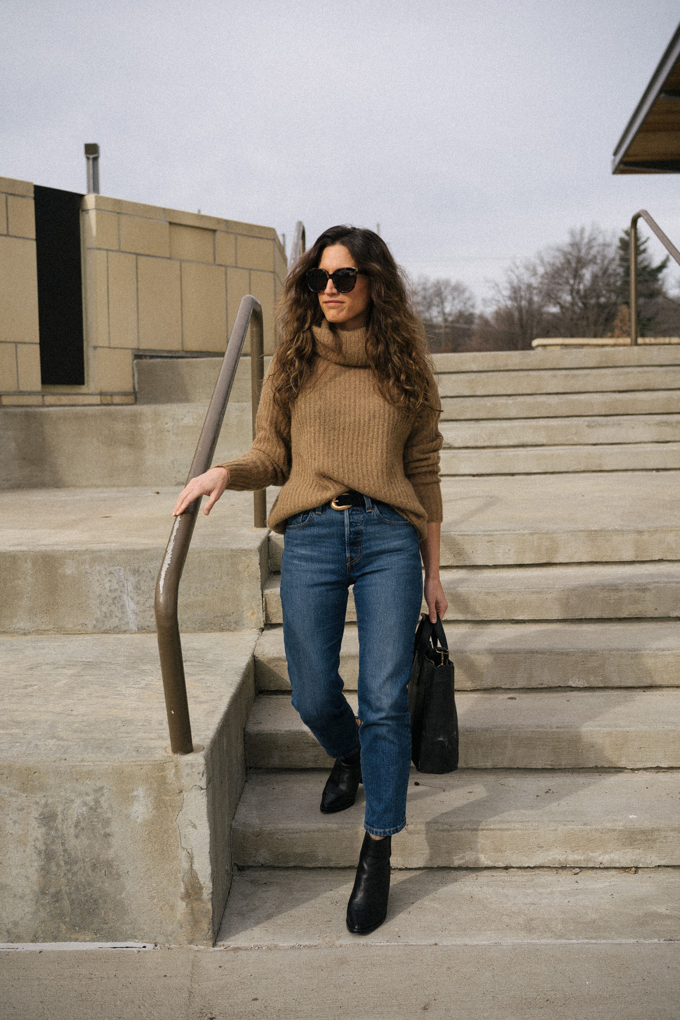 ashley wearing a brown turtleneck sweater, dark wash denim, and black boots