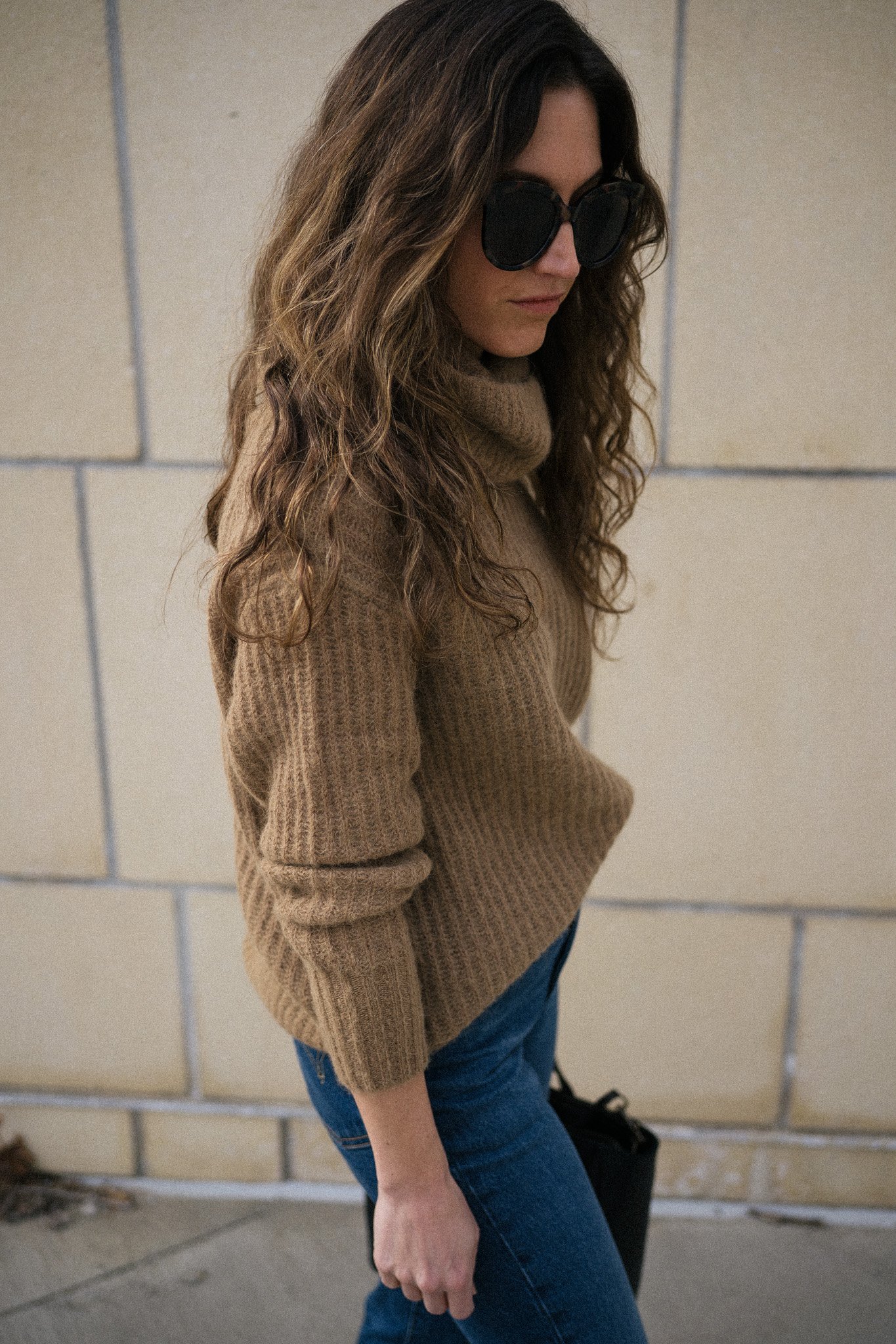 ashley wearing a brown turtleneck sweater, dark wash denim, and black boots