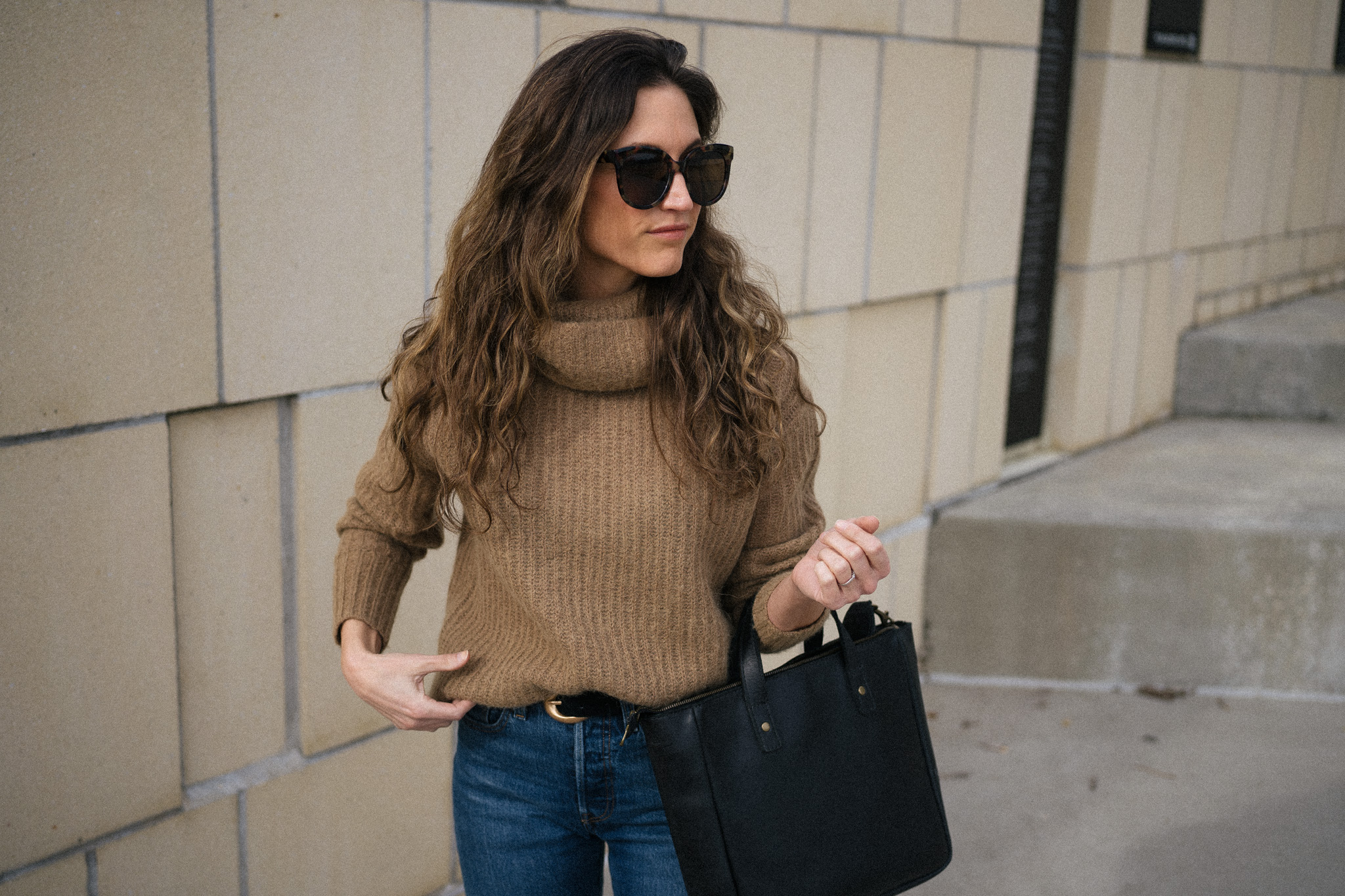 ashley wearing a brown turtleneck sweater, dark wash denim, and black boots
