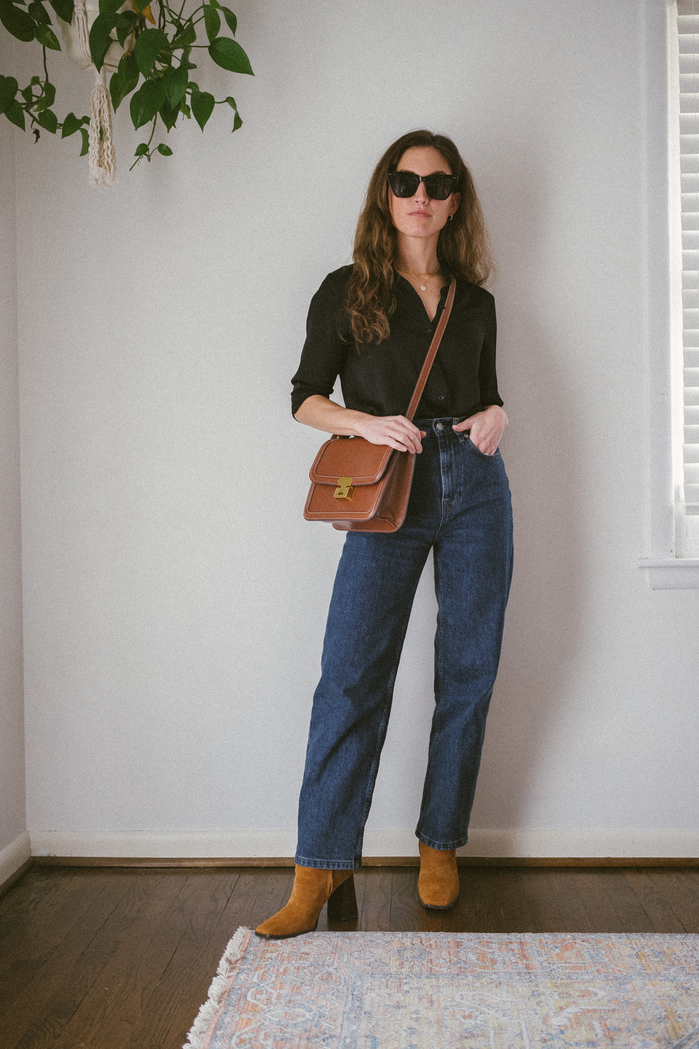 winter capsule wardrobe outfit with a black silk button down, dark wash straight denim, and brown boots