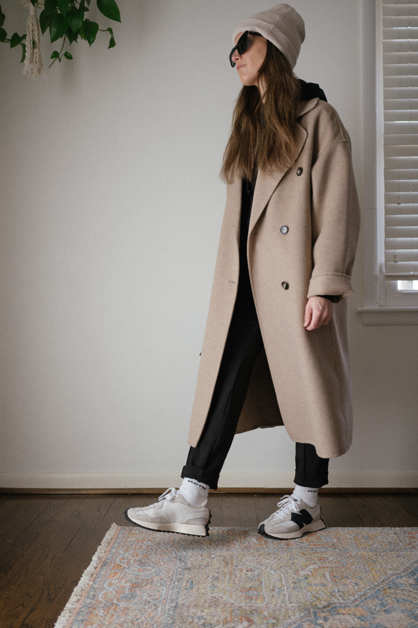 winter outfit with a black hoodie, black pants, a beige oversized coat, and casual sneakers