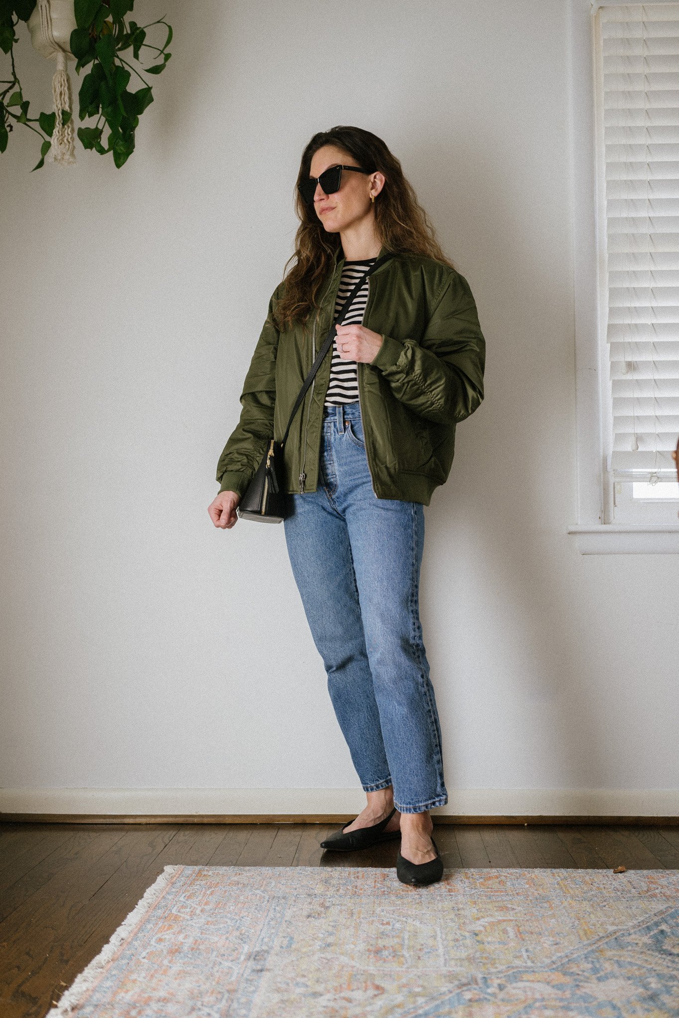 early spring outfit with a striped tee, green bomber jacket, midwash denim, and black slingback flats