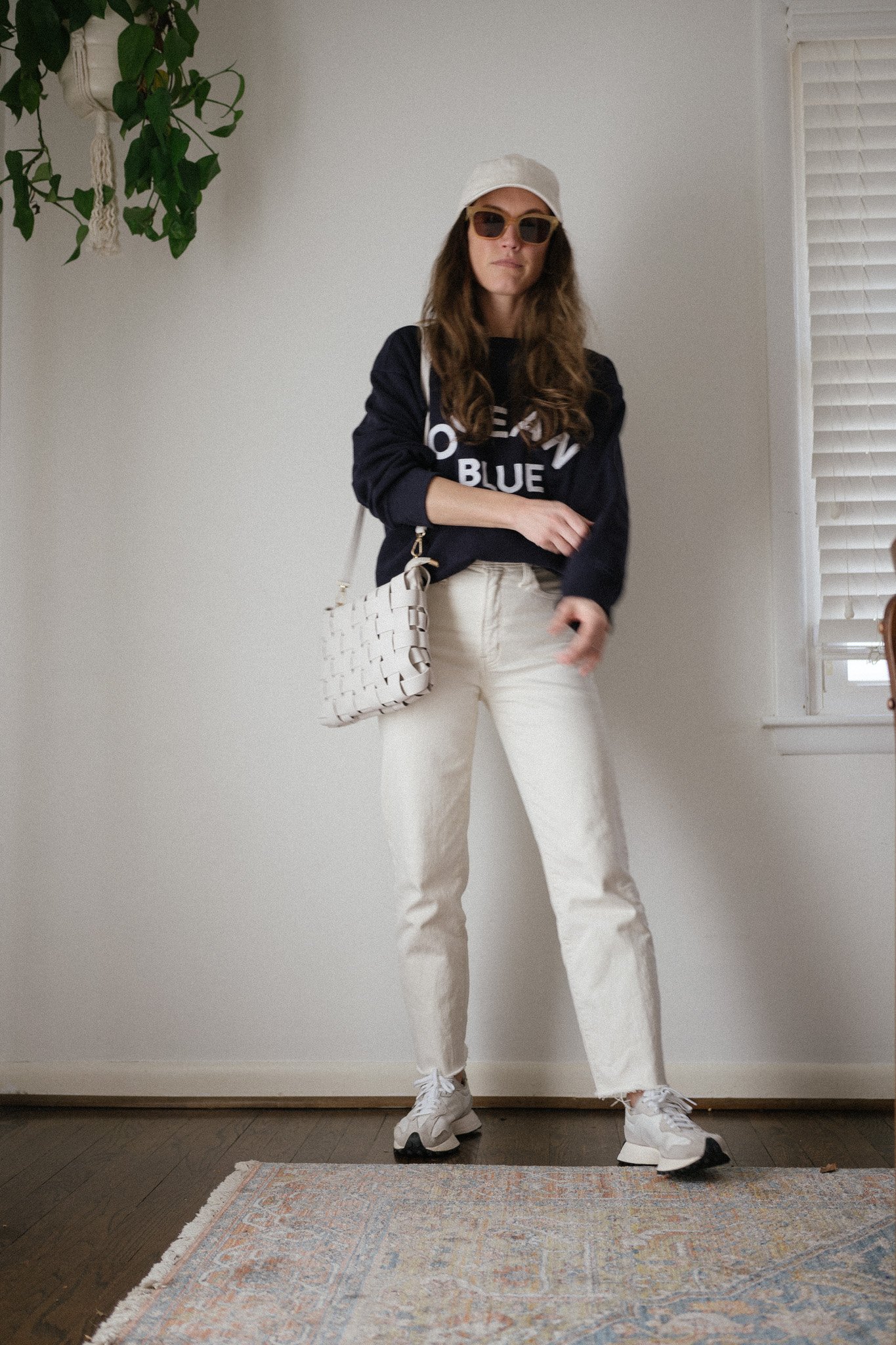 early spring outfit with a navy graphic sweatshirt, white denim, and casual sneakers