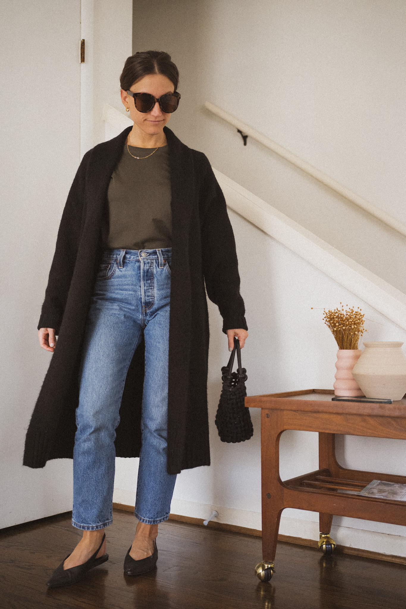daily look with a green tee, black sweater coat, medium wash straight denim, and black slingback flats