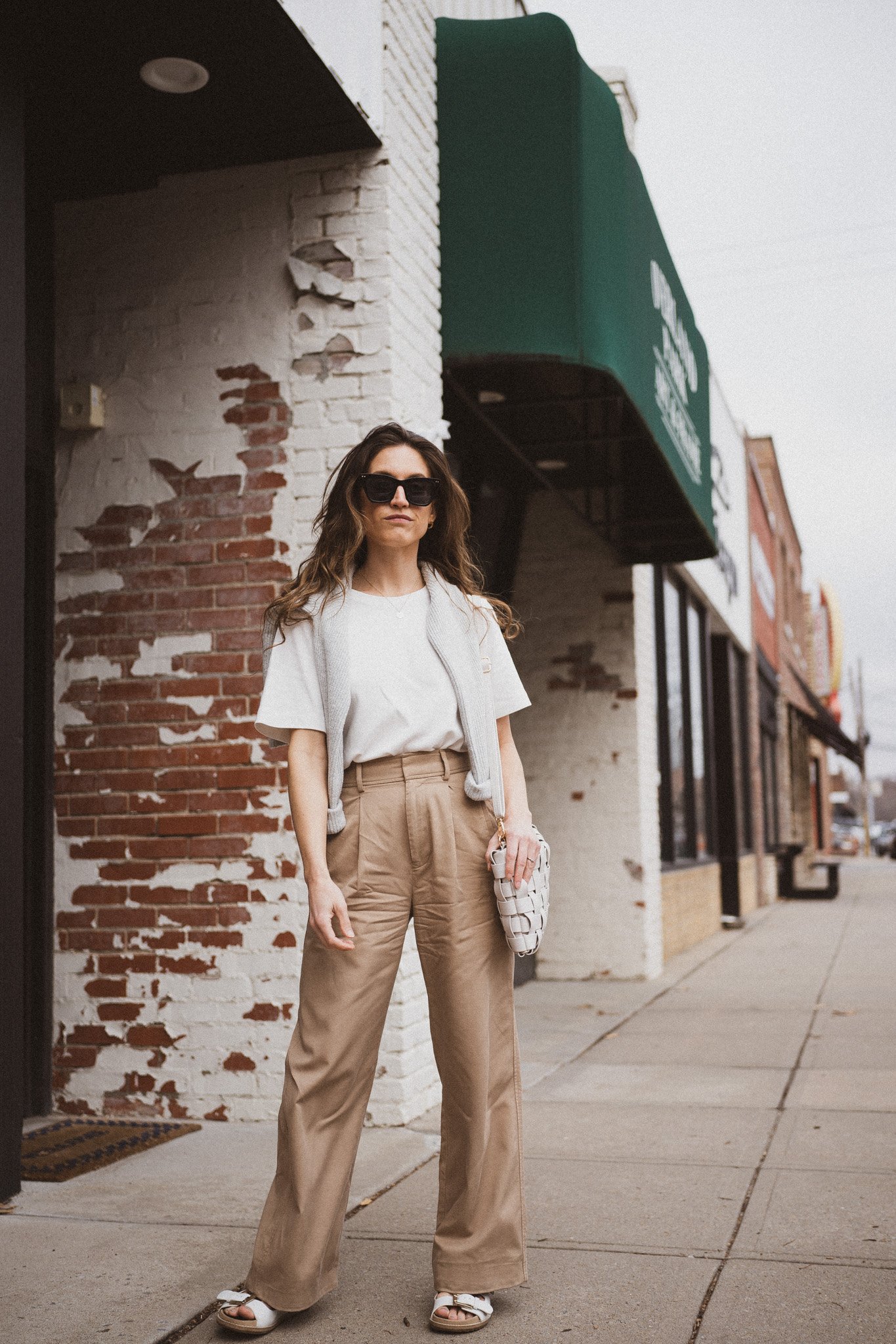 spring outfit idea with a white tee, gray sweater worn over the shoulders, wide leg trousers, and white footbed sandals