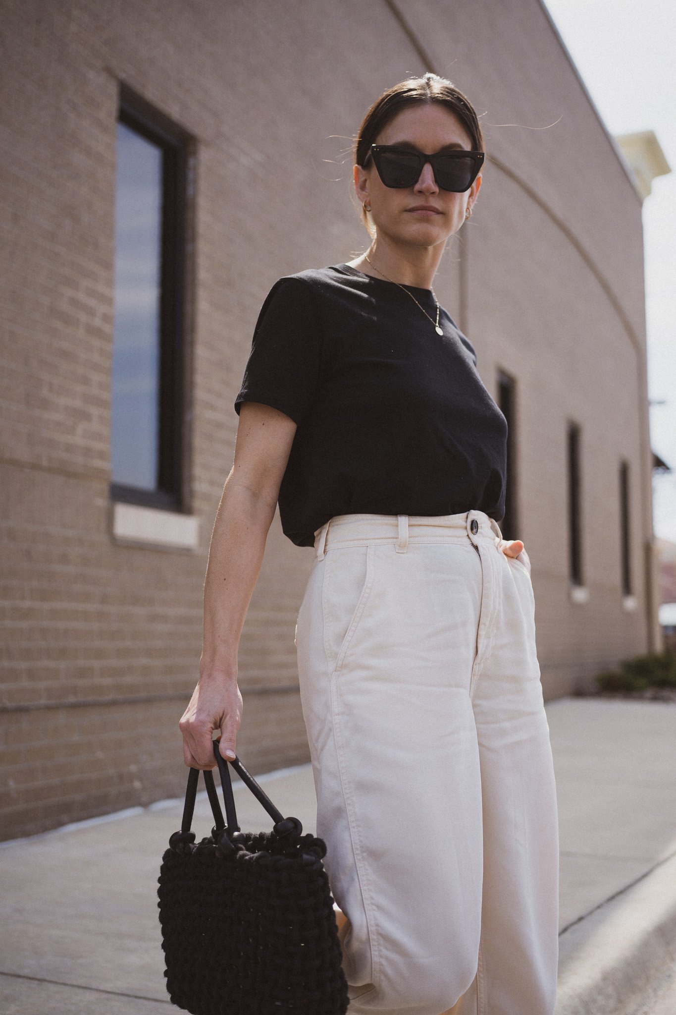 ashley wearing  a black tee, beige chino pants, and black slingback flats standing next to a gray building