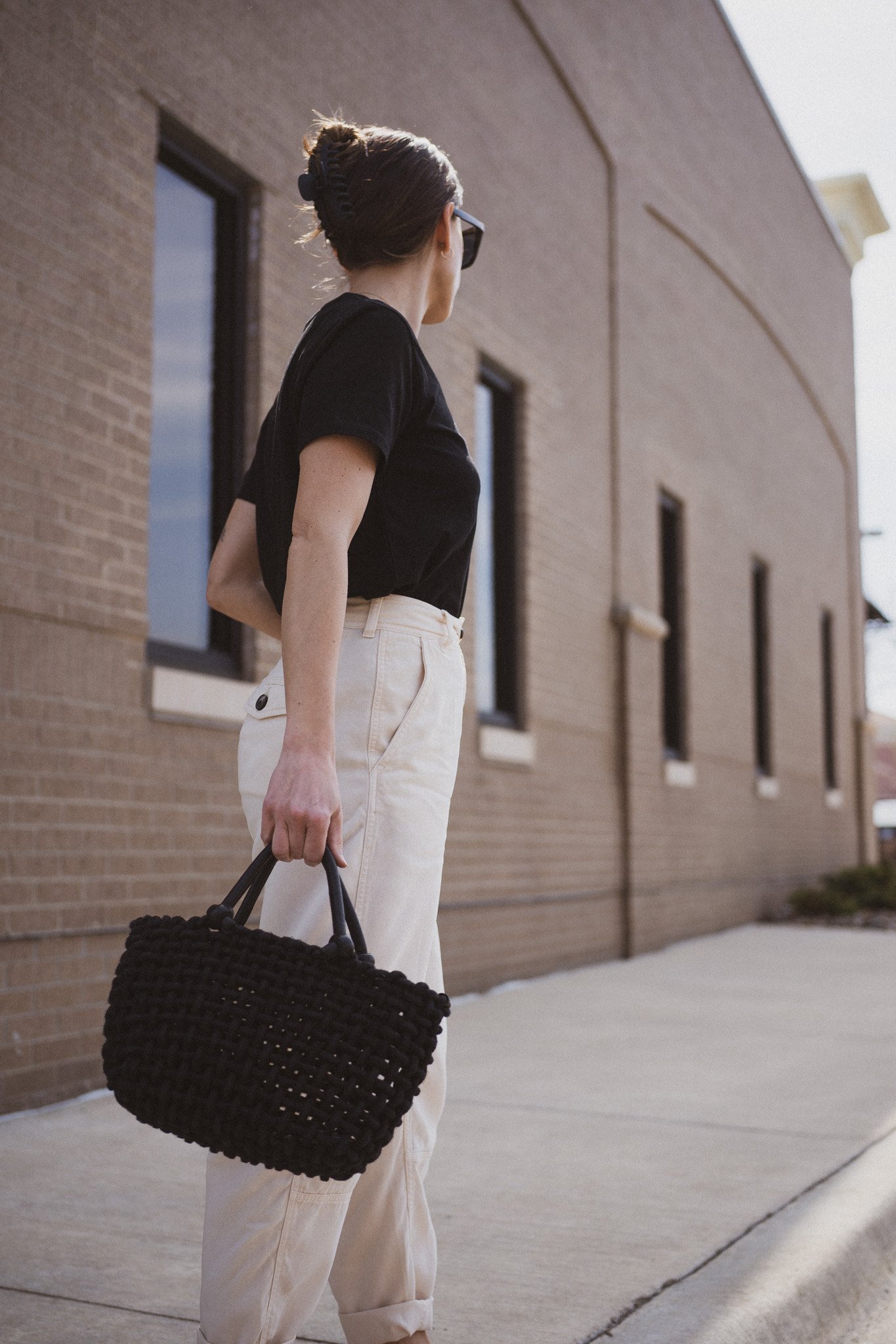 ashley wearing  a black tee, beige chino pants, and black slingback flats standing next to a gray building