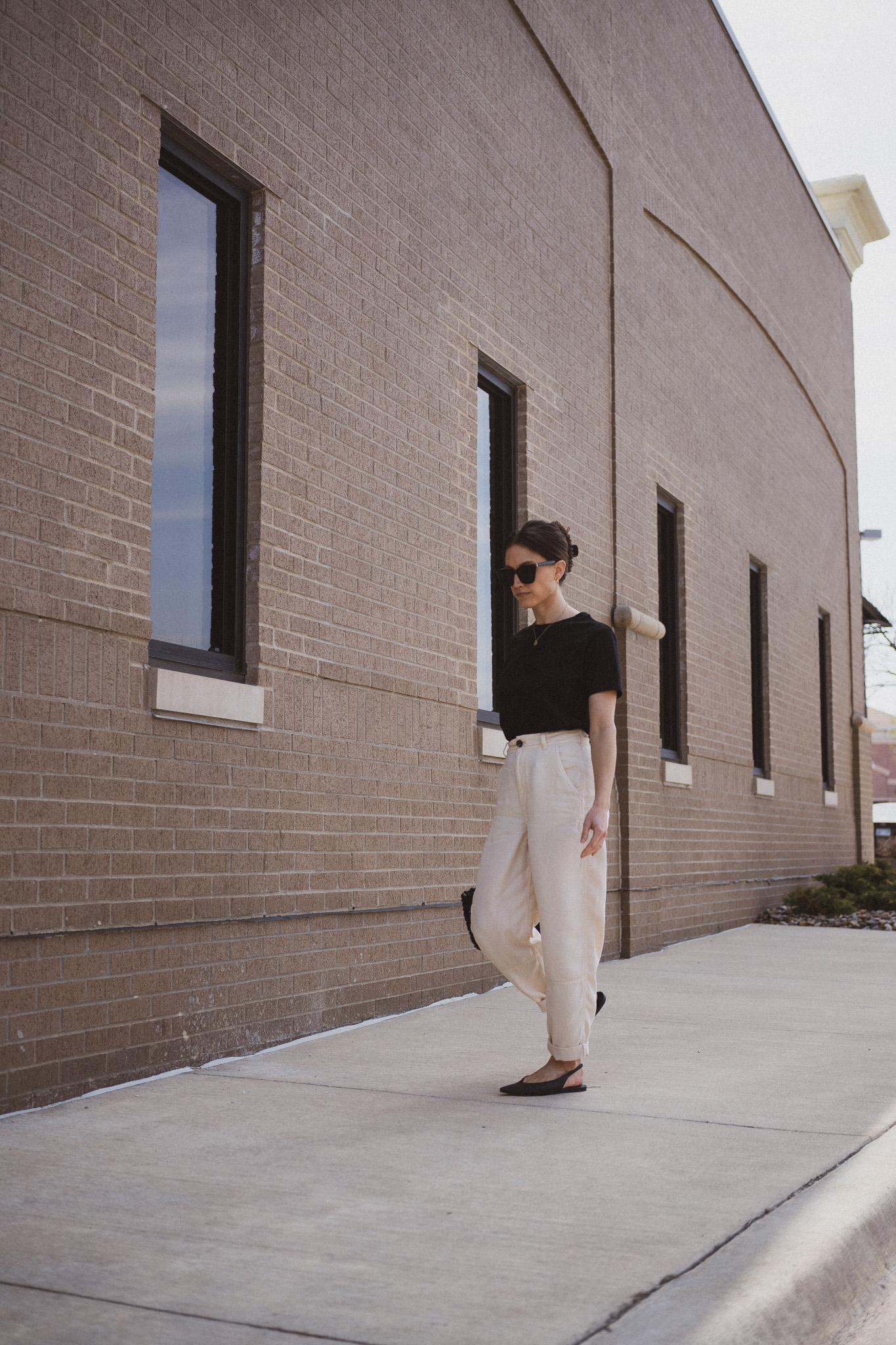 ashley wearing  a black tee, beige chino pants, and black slingback flats standing next to a gray building