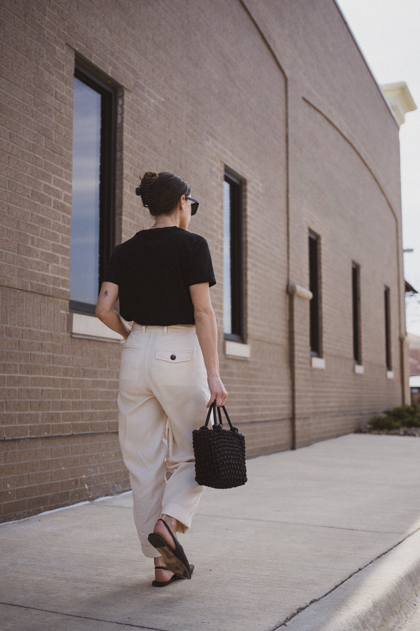 ashley wearing  a black tee, beige chino pants, and black slingback flats standing next to a gray building