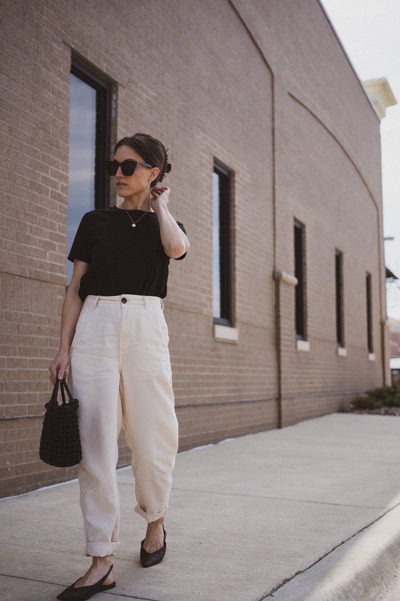 ashley wearing  a black tee, beige chino pants, and black slingback flats standing next to a gray building