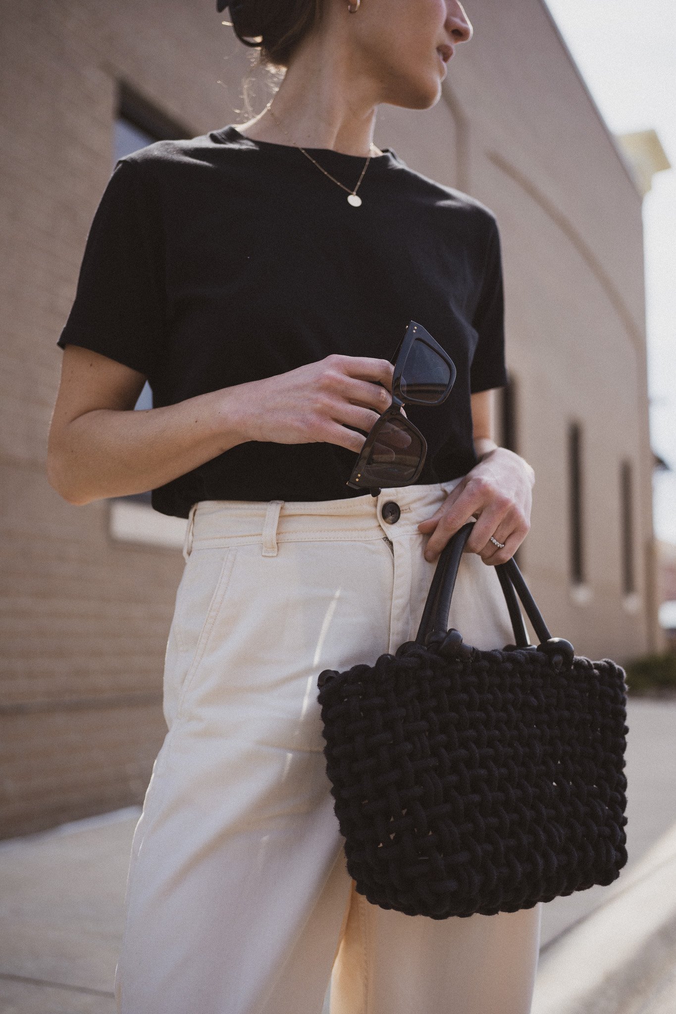 ashley wearing  a black tee, beige chino pants, and black slingback flats standing next to a gray building