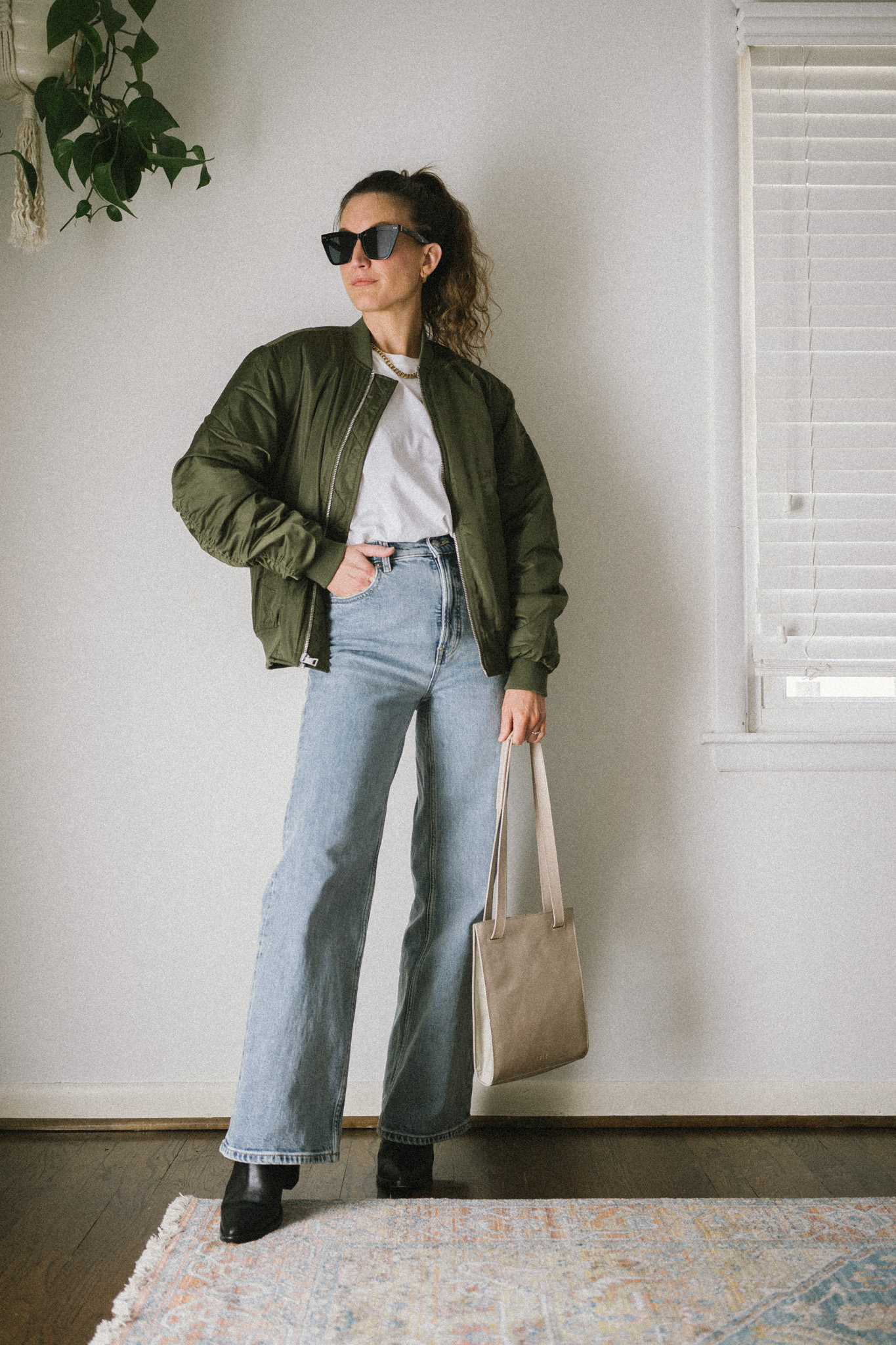 spring outfit idea with a white tee, green bomber jacket, wide leg denim, and black boots