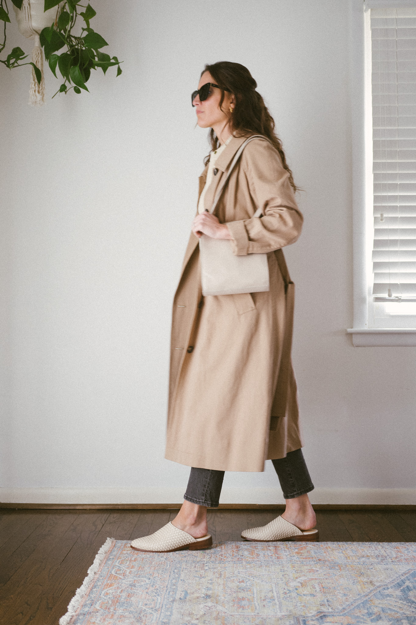 ashley wearing a tan trench coat, black denim, and white woven mules