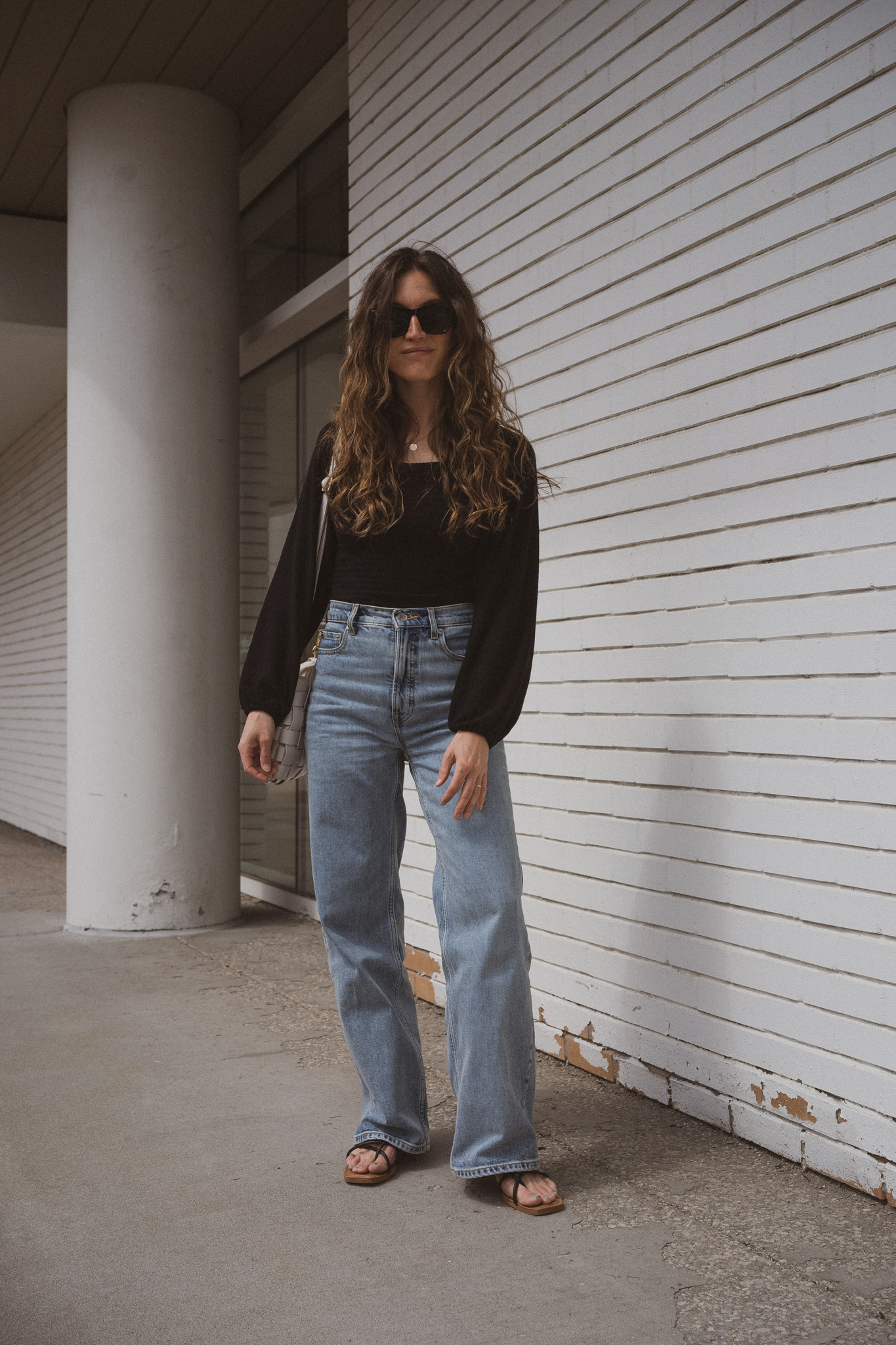 spring outfit with a black smocked blouse, wide leg jeans and strappy black sandals