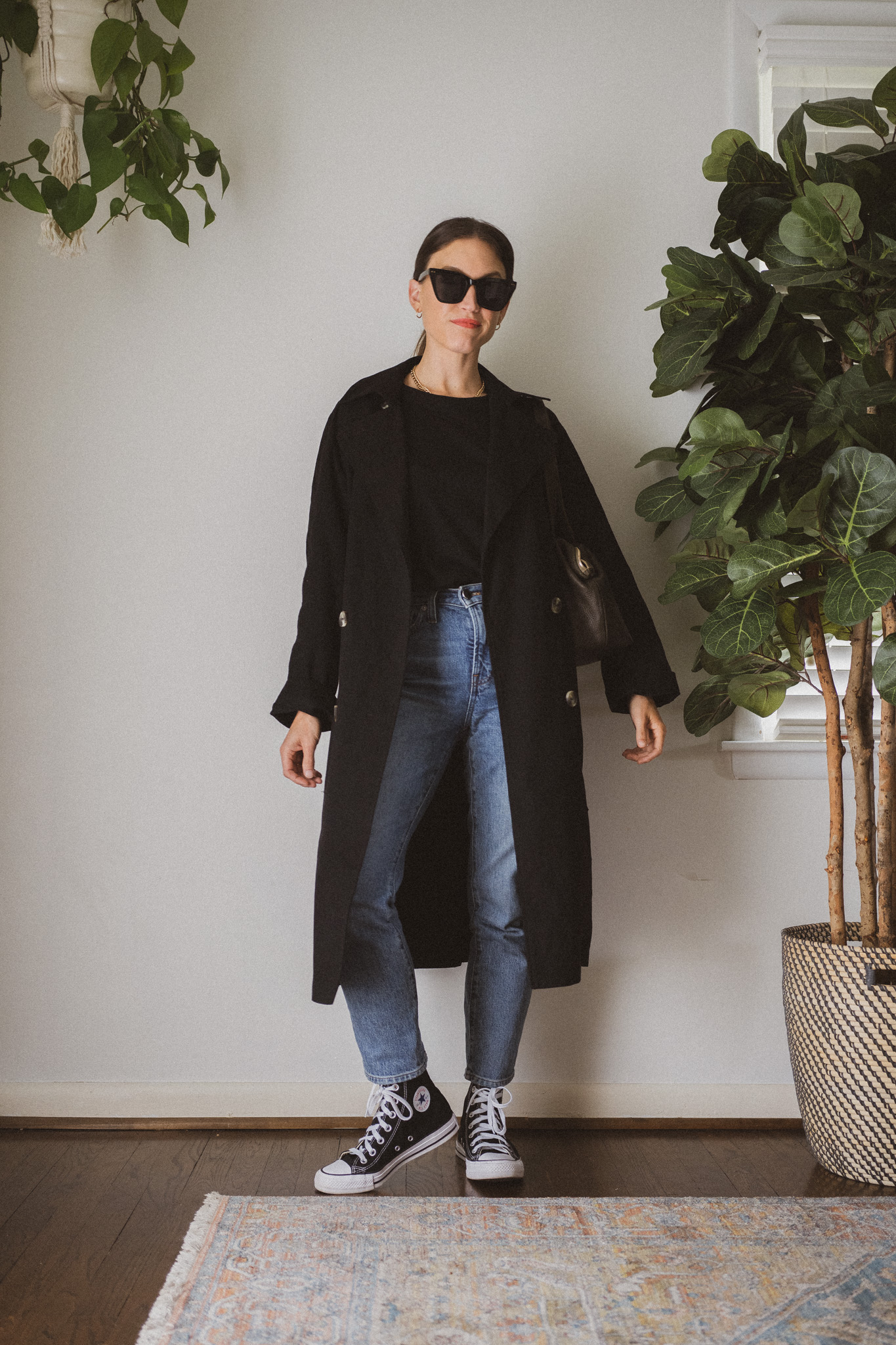 rainy day spring look with a black tee, black trench coat, medium wash denim, and black high top Converse