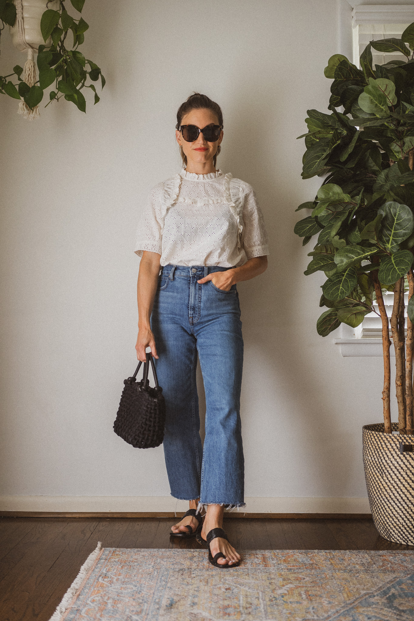 spring look for 2023 with an eyelet blouse, medium wash jeans, and black sandals