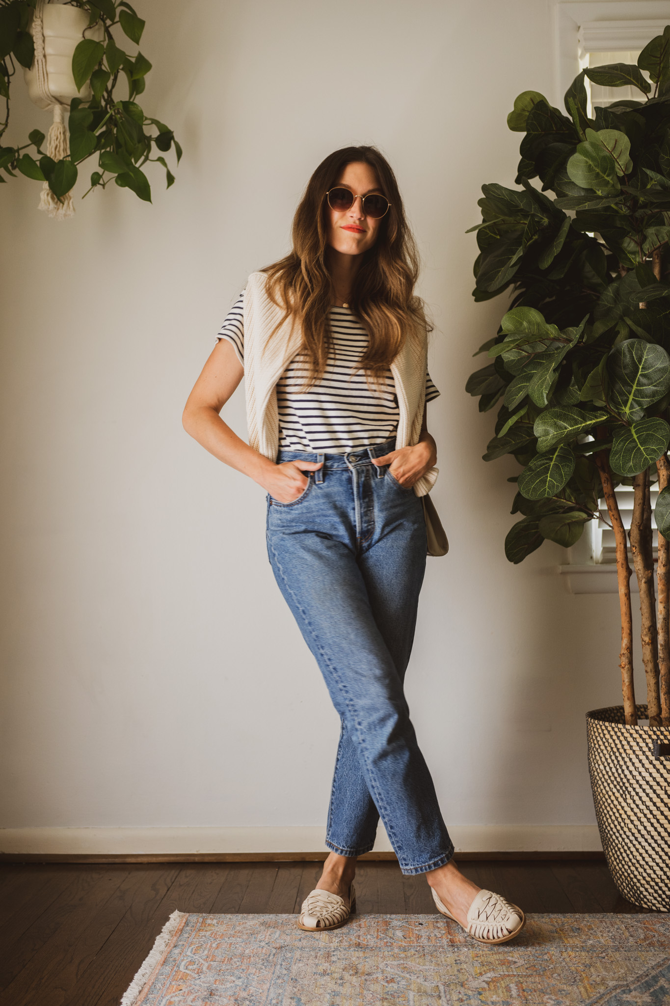 spring look for 2023 with a striped tee, cream sweater worn over the shoulders, medium wash denim, and huarache sandals