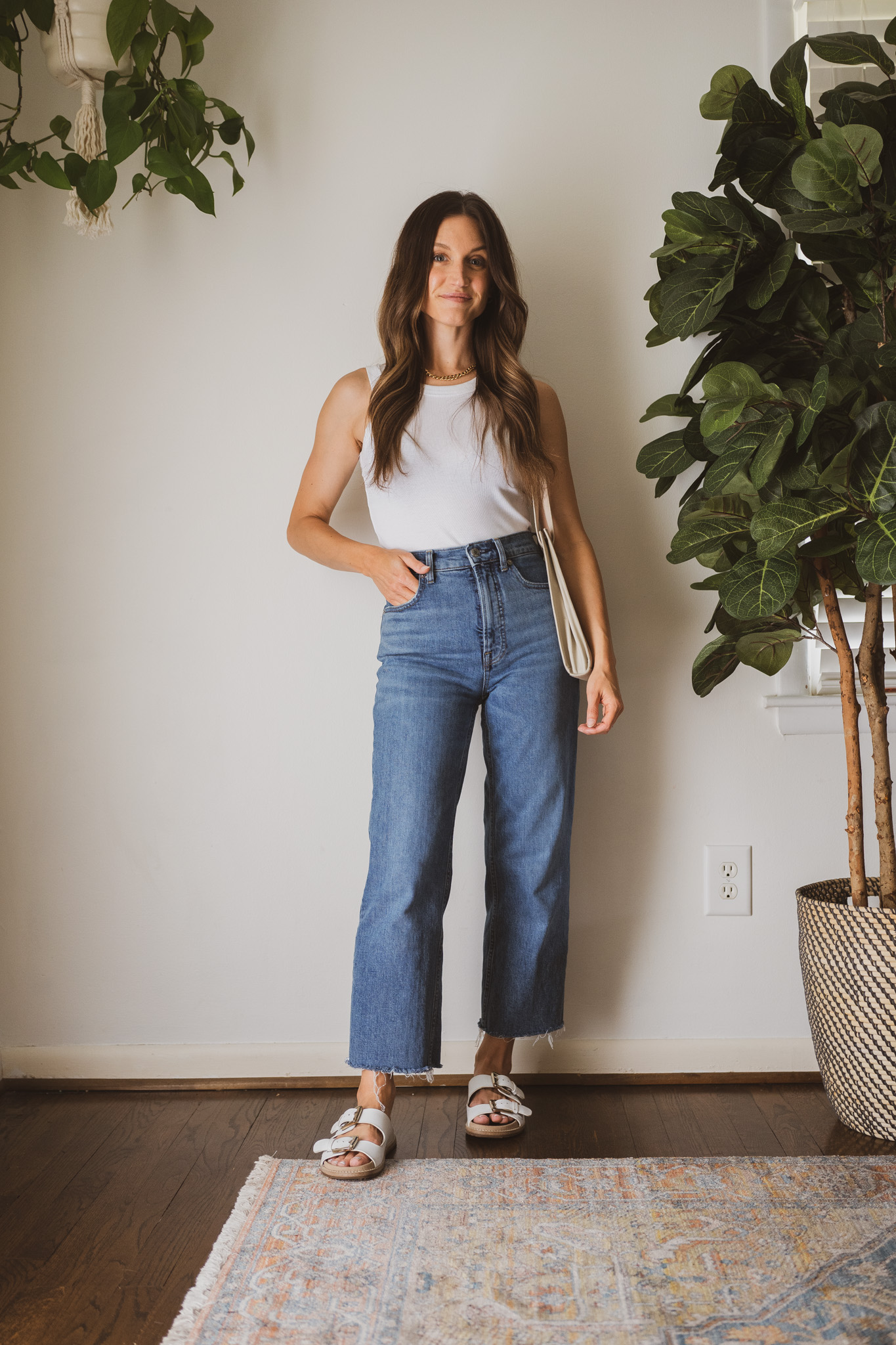 minimal outfit with a white tank, medium wash straight denim, white sandals, and a gray shoulder bag