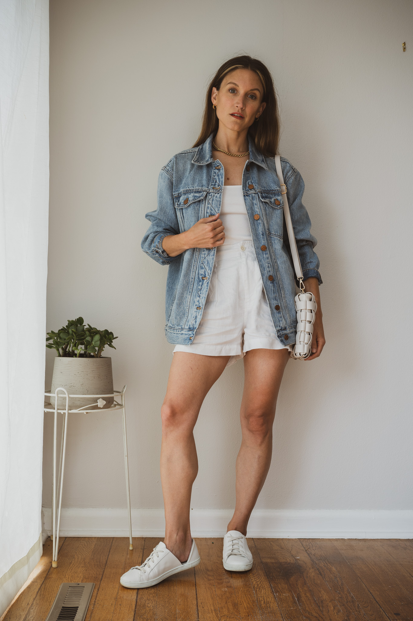 minimal outfit with a white tank, white linen shorts, white sneakers, and an oversized denim jacket