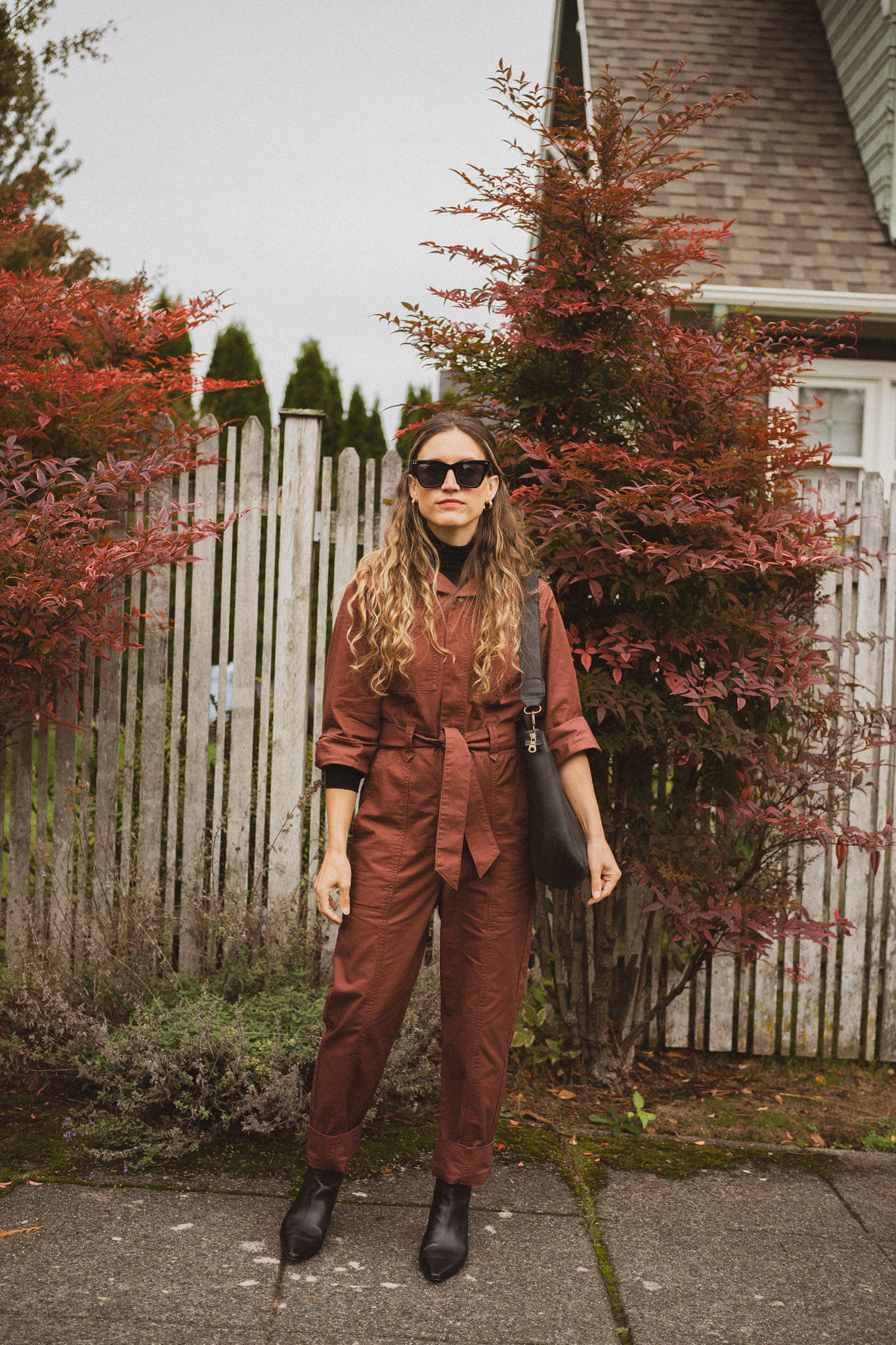 fall outfit idea with a jumpsuit, black turtleneck layered underneath, and black boots with a black tote bag, and black cat eye sunglasses